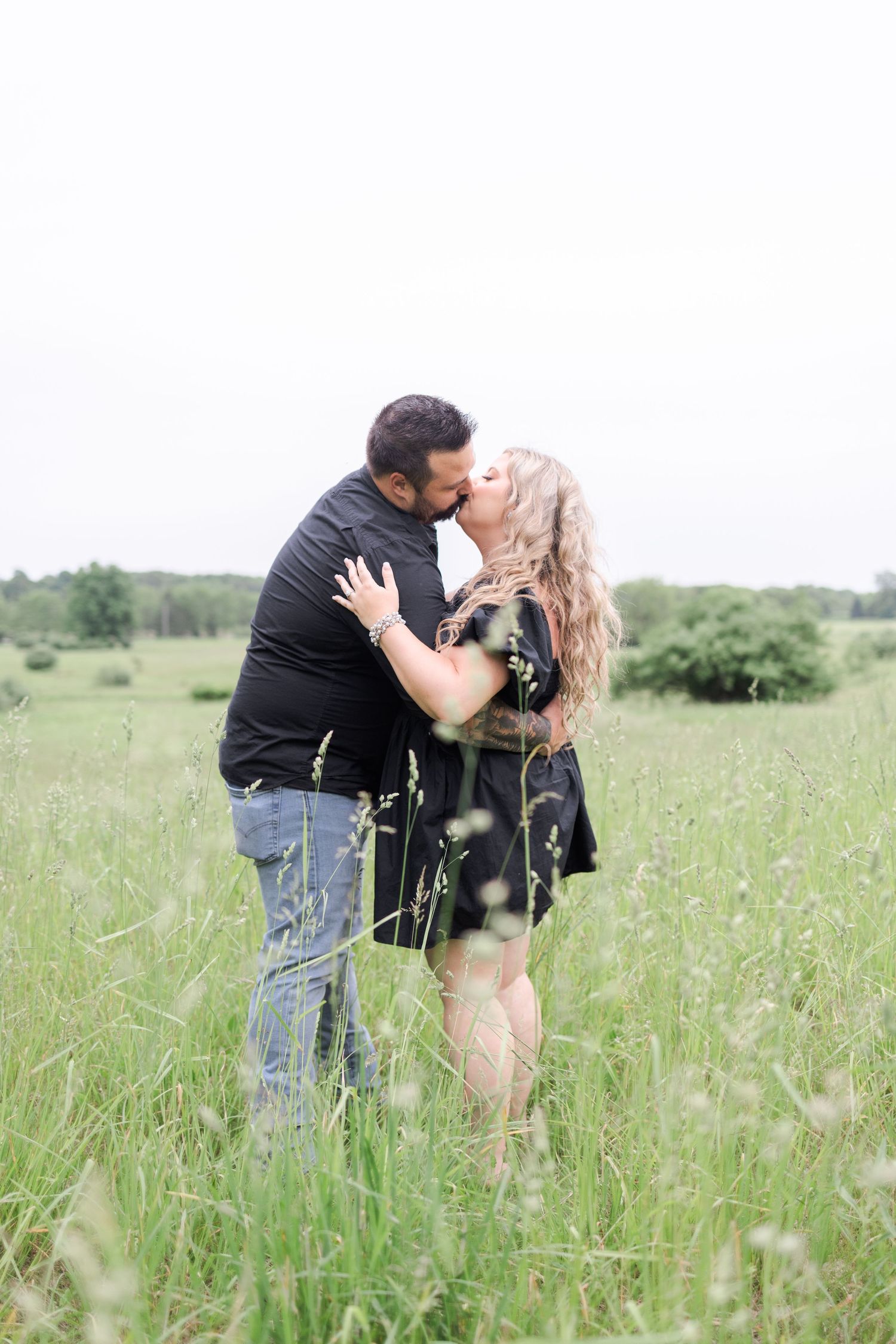 A couple shares romantic kisses while standing among wildflowers in a meadow.