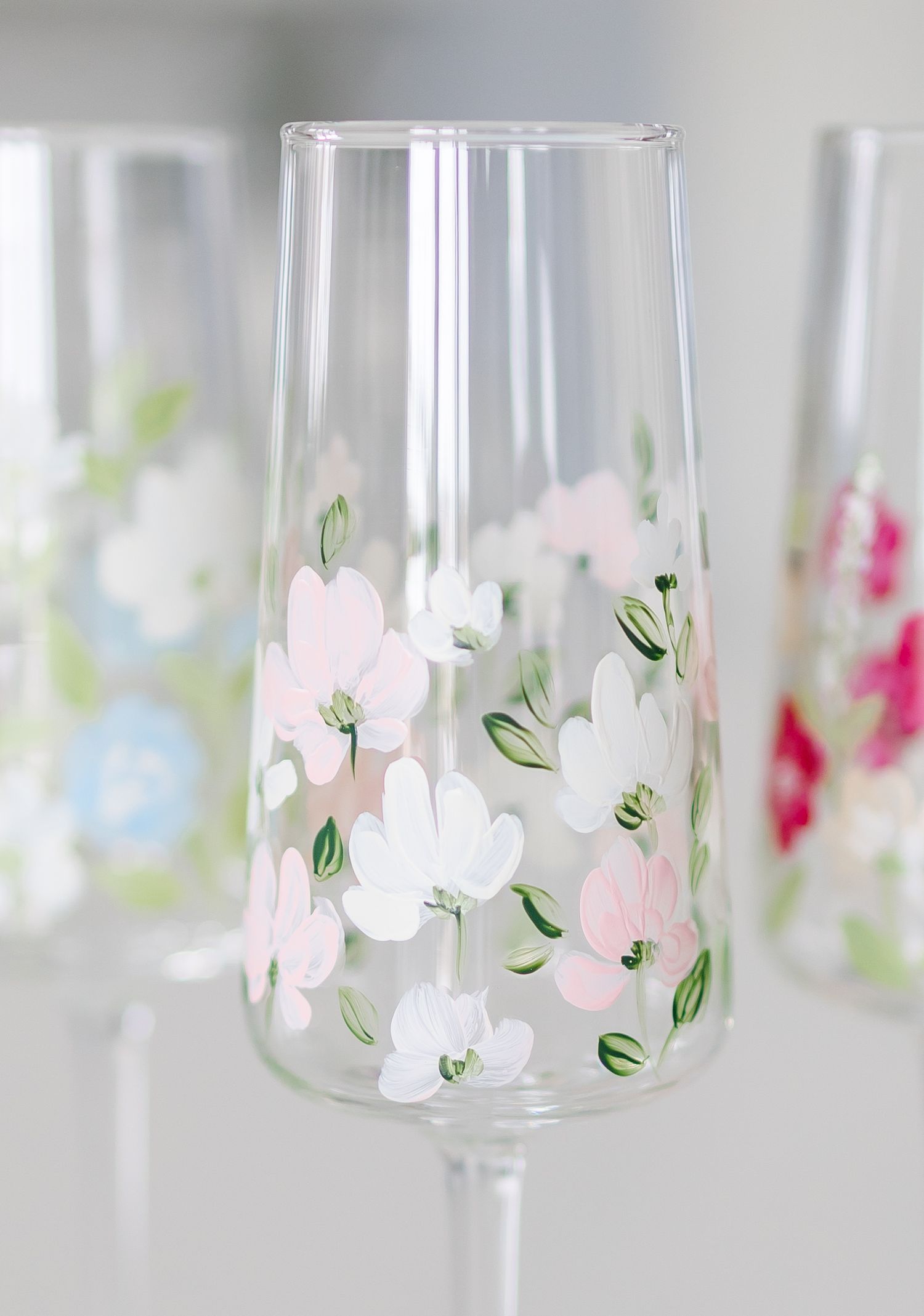 Clear glass stemware with delicate hand-painted pink and white floral designs and green leaves decorating the sides.