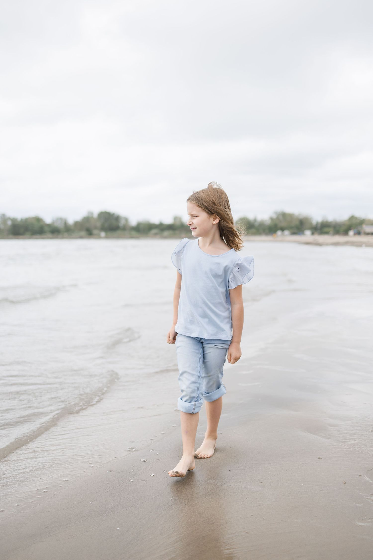 Person walking along wet sand at beach wearing casual blue clothing.