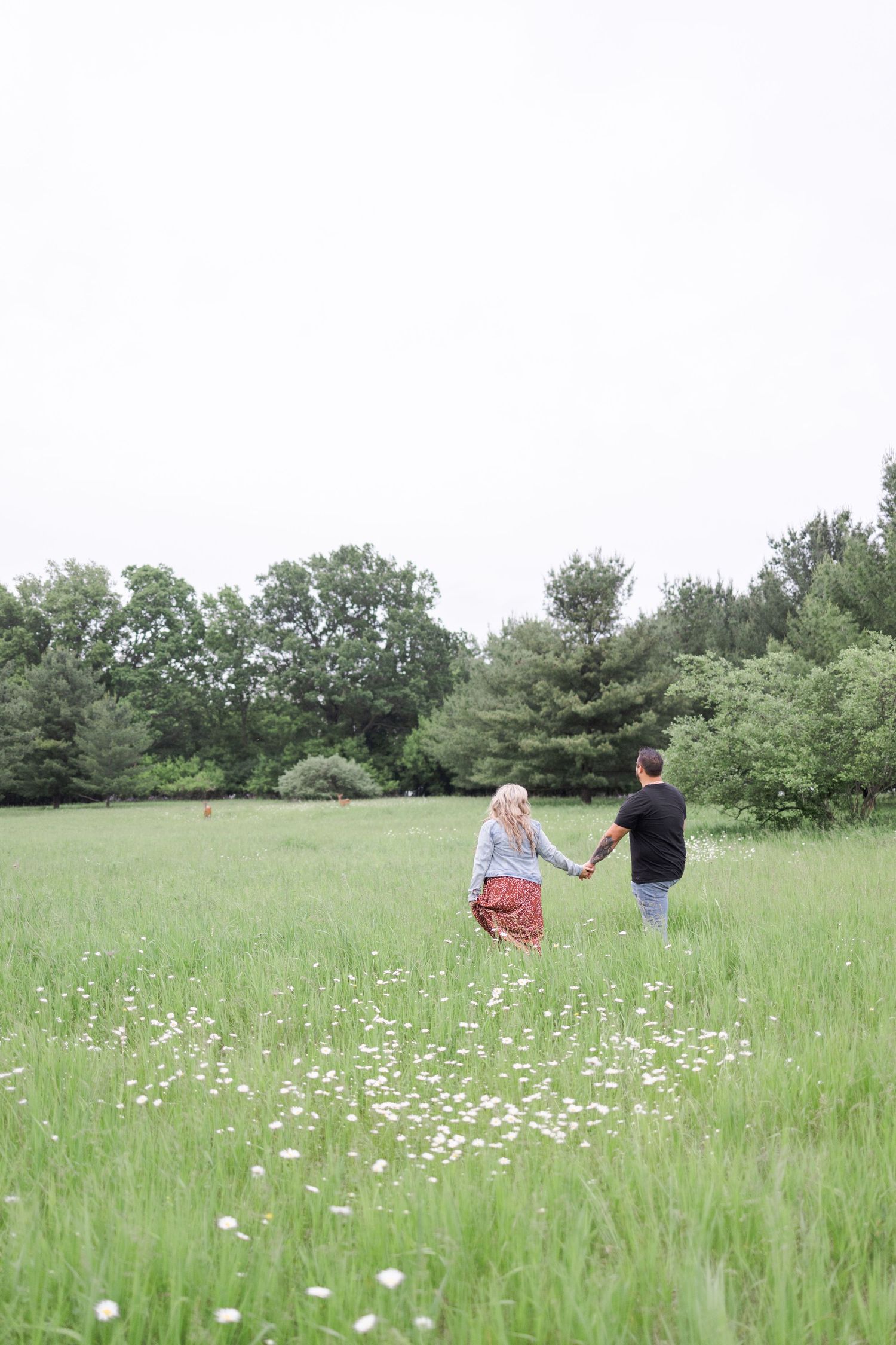 Couple walking through a meadow filled with white wildflowers on a bright summer day.