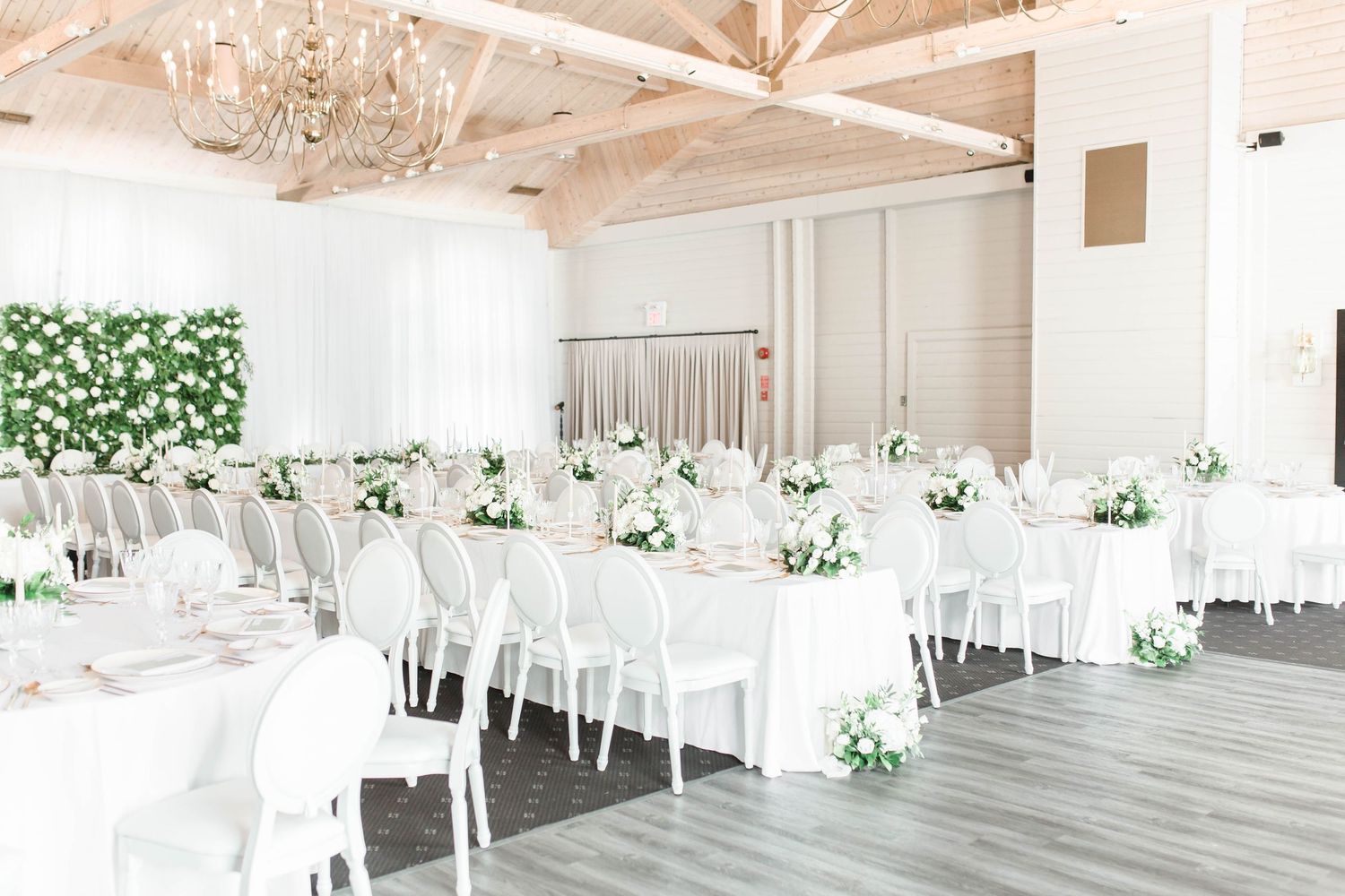 Light and airy wedding reception venue with white tables, chairs and floral arrangements under a crystal chandelier.