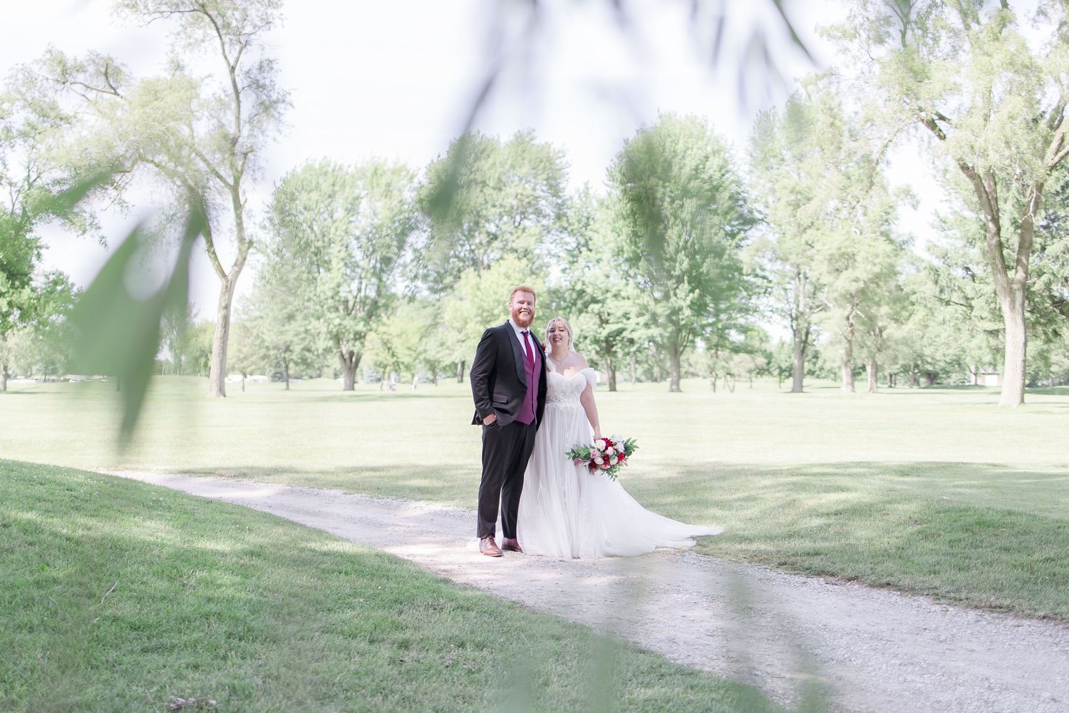 Distant view of wedding couple walking along garden path surrounded by trees.