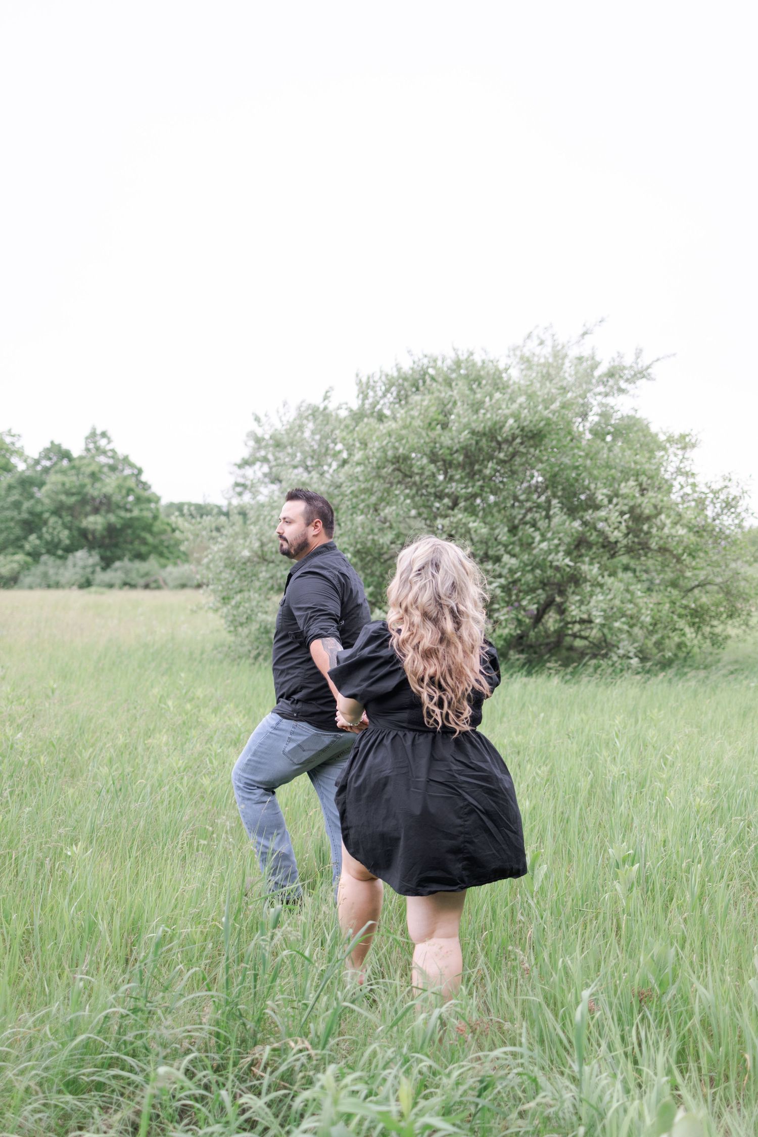 A playful couple runs through a grassy meadow during an outdoor photoshoot.
