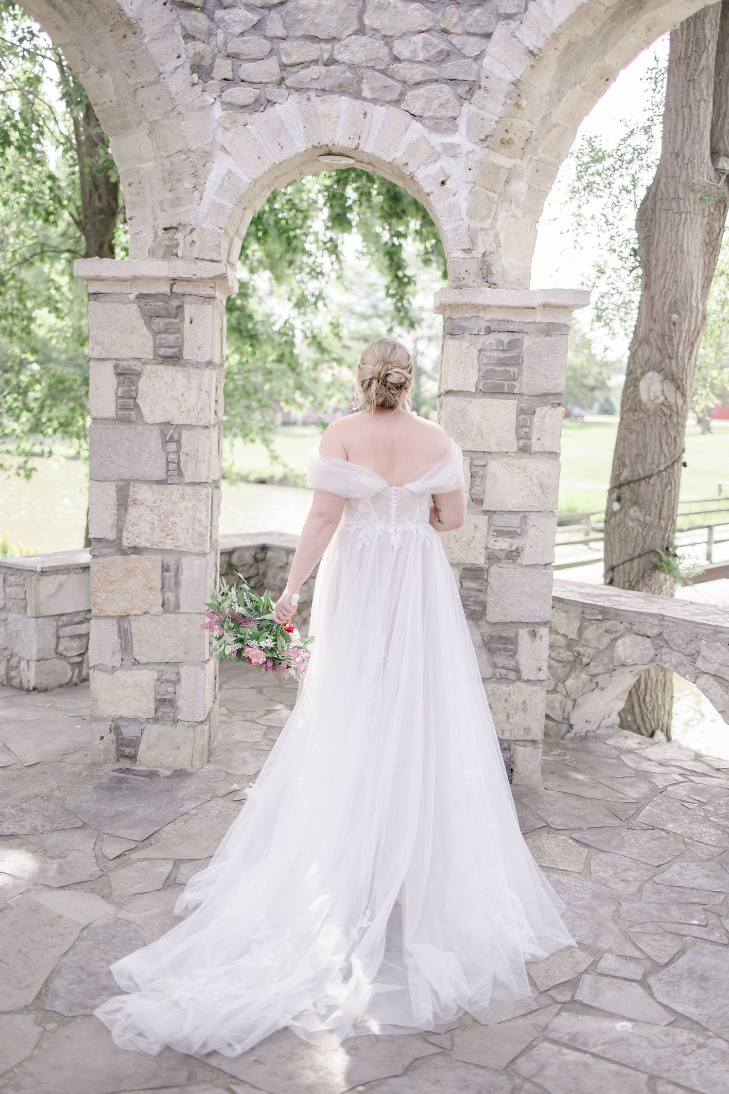 A flowing white wedding dress train trails across a stone patio beneath elegant archways.