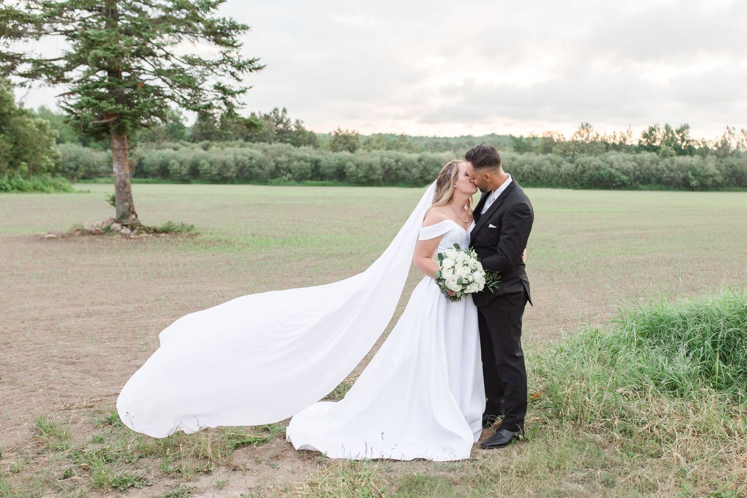 Romantic wedding couple embracing in field with dramatic flowing white dress train.