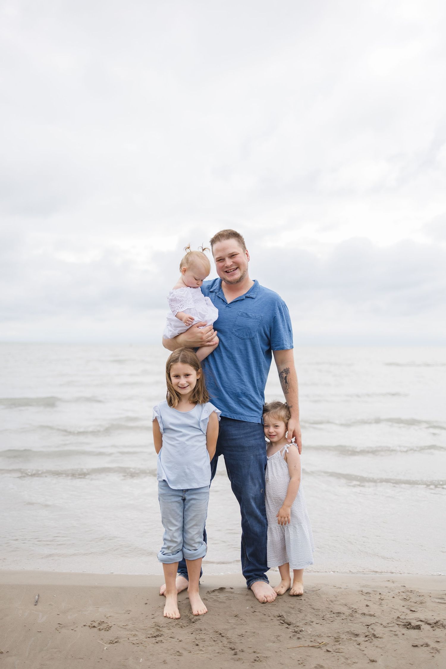 Family of four posing together on beach in coordinated blue and white clothing.