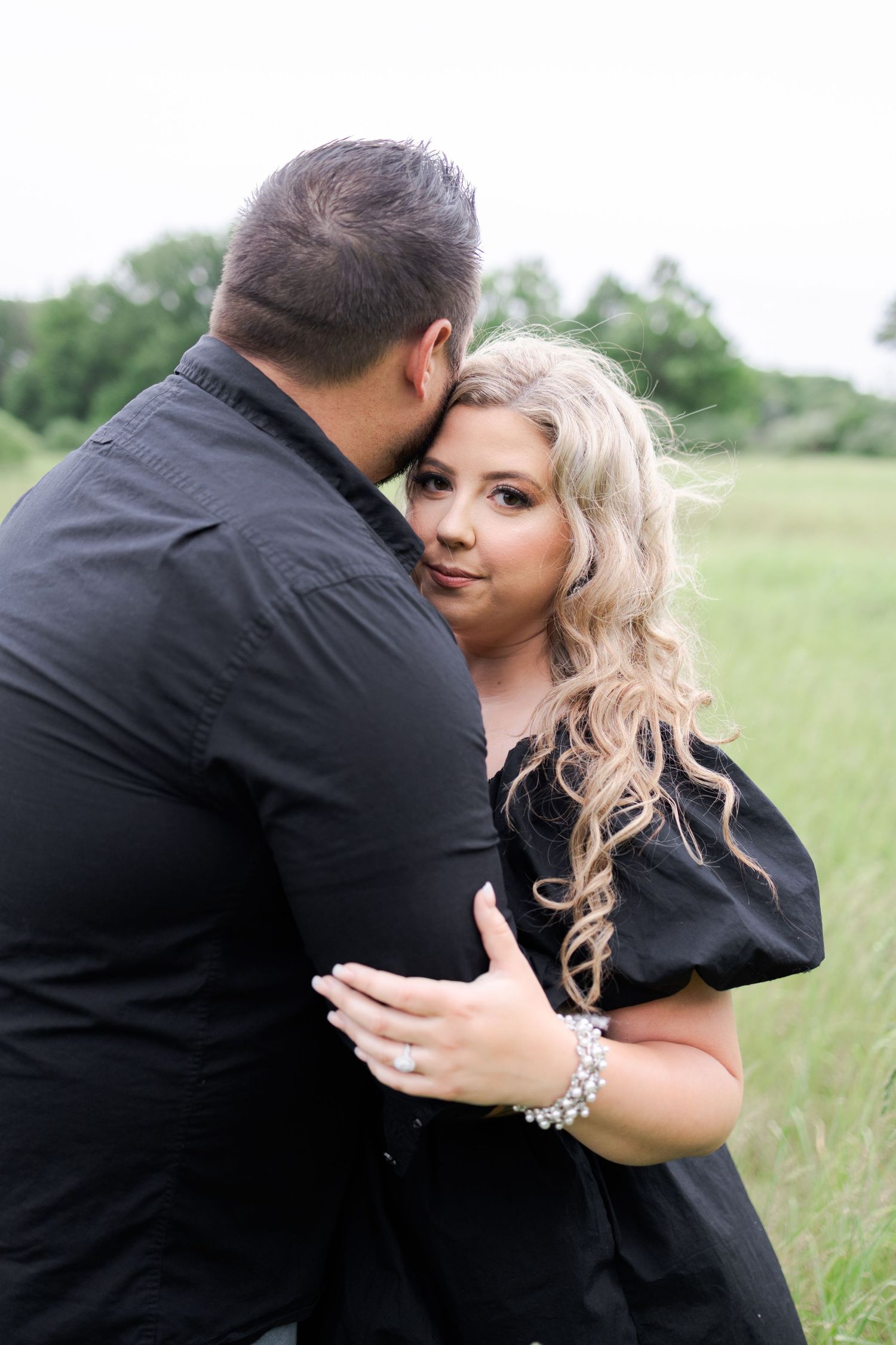 Couple in black clothing embraces tenderly in a green summer field.