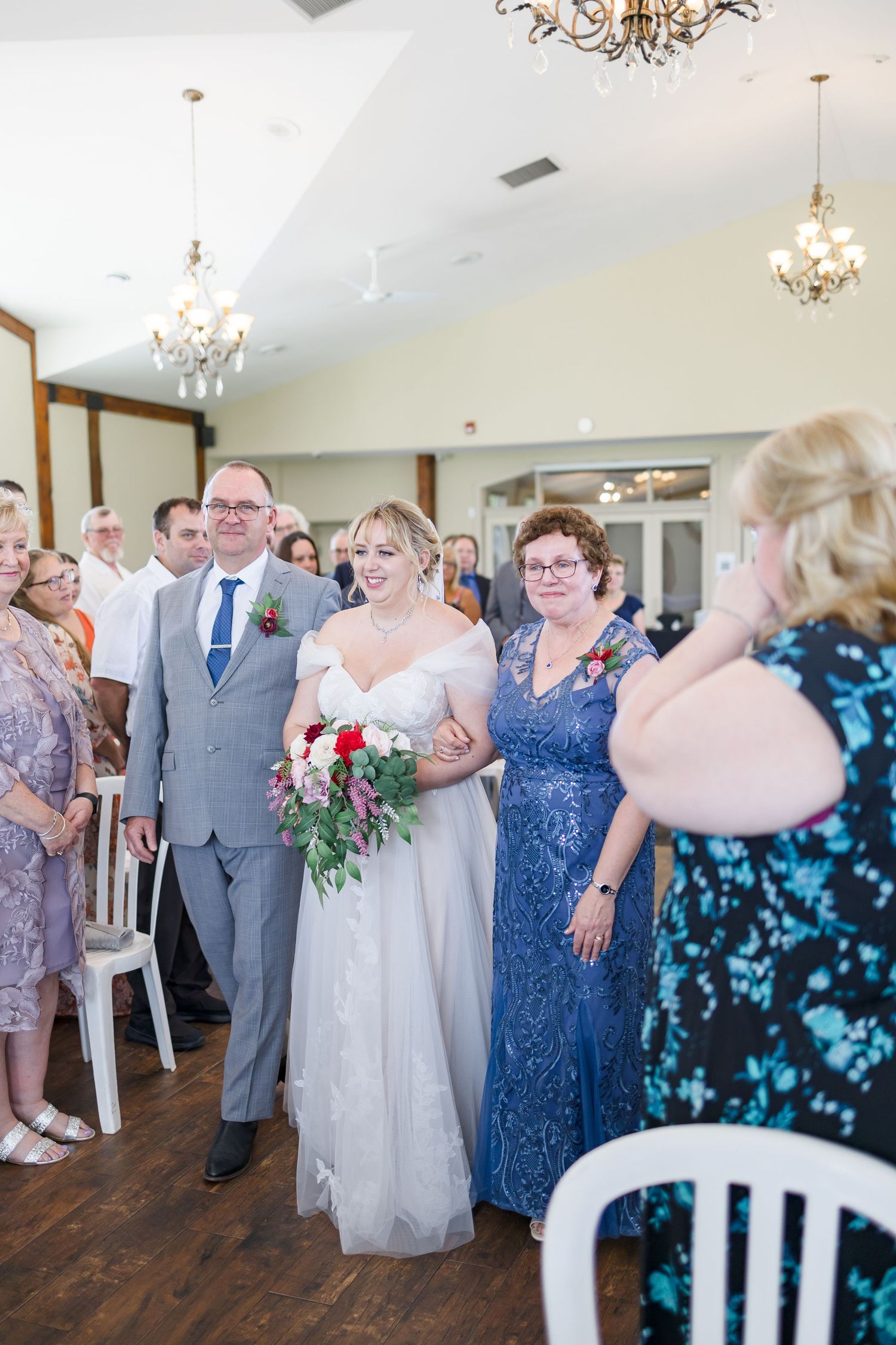 Wedding party and guests gather for dancing in an elegant venue with hardwood floors.
