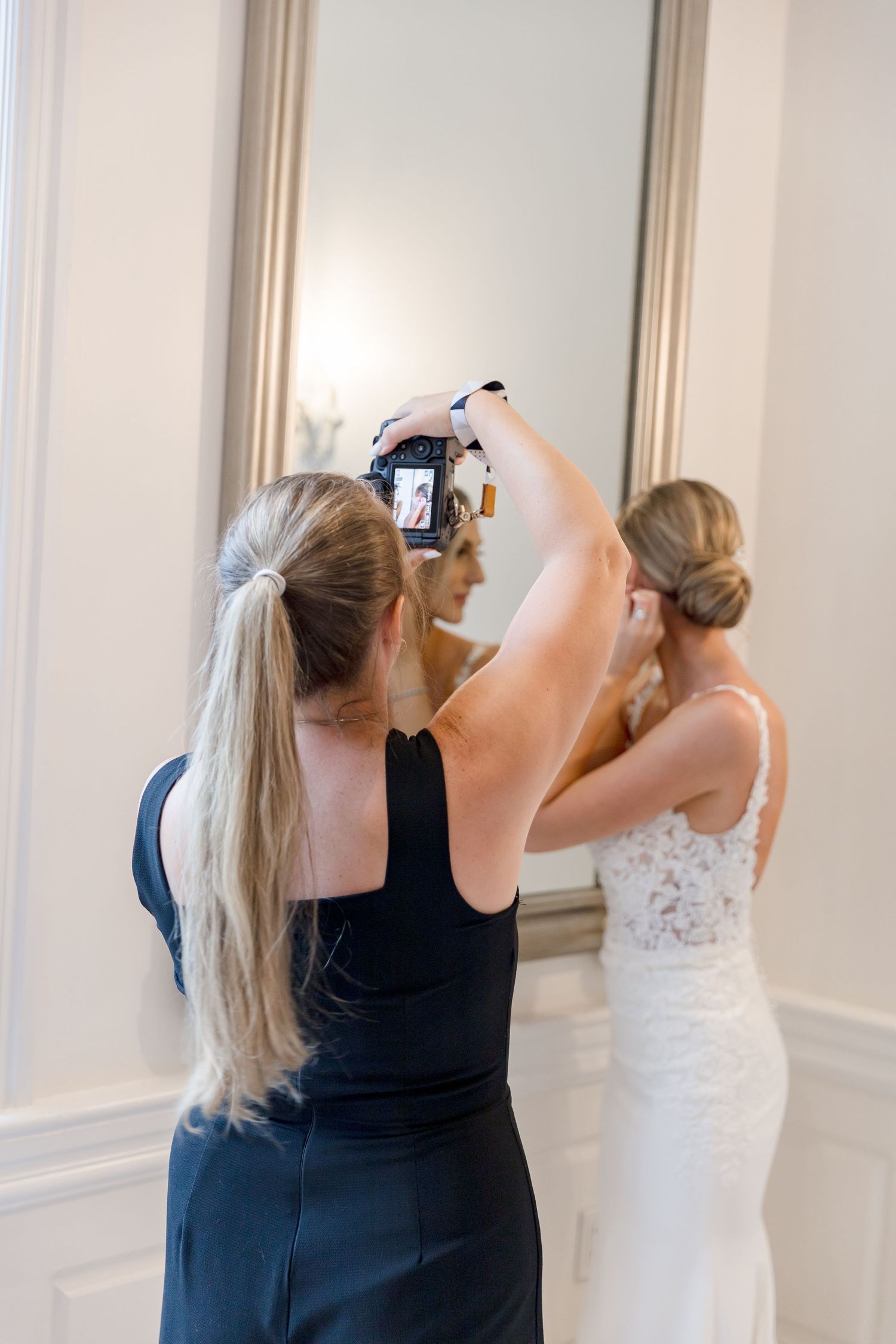 A photographer takes photos of a bride getting ready in front of an elegant mirror.
