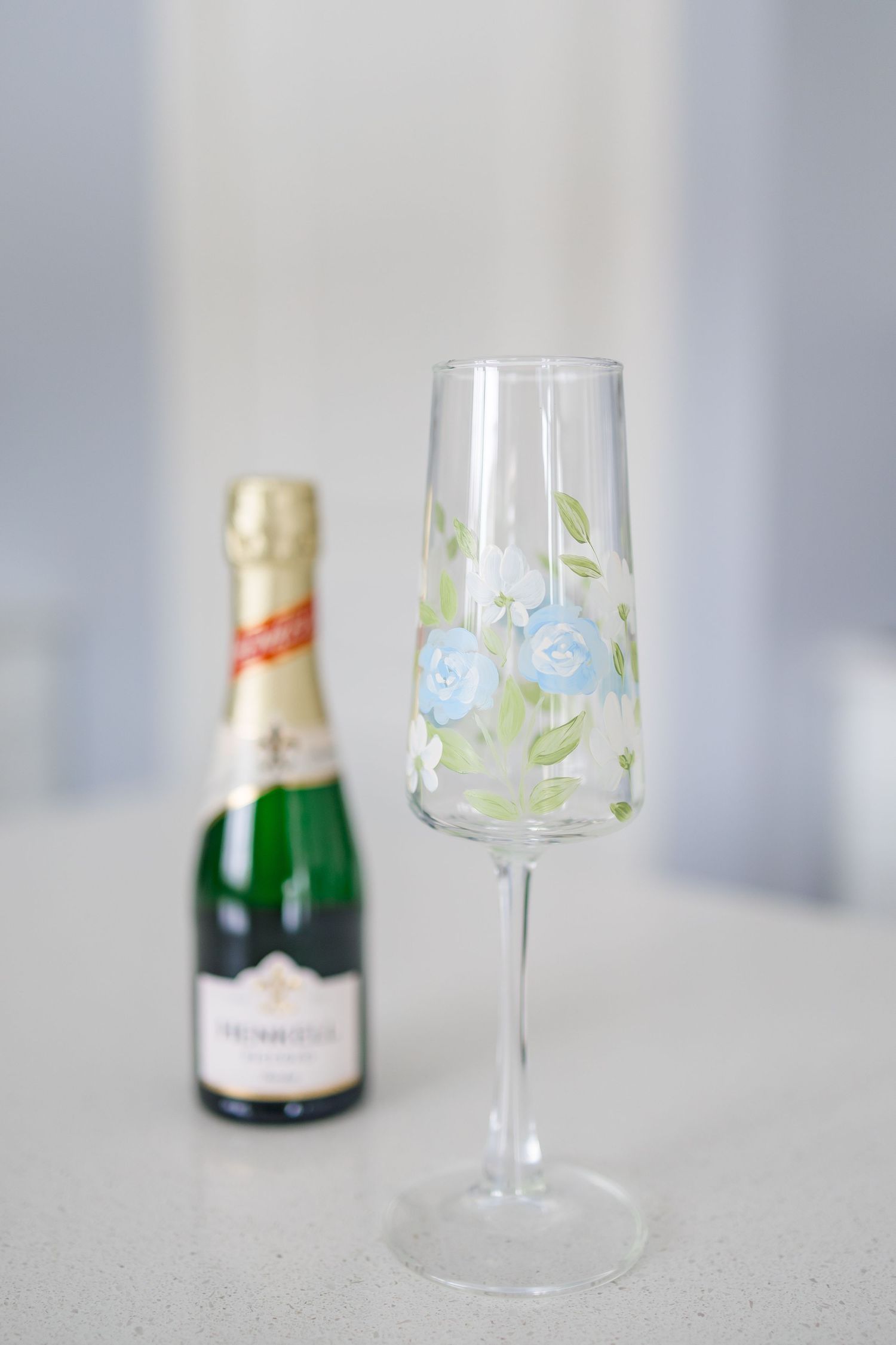 A champagne bottle with elegant wine glasses featuring delicate blue floral designs on a light gray background.