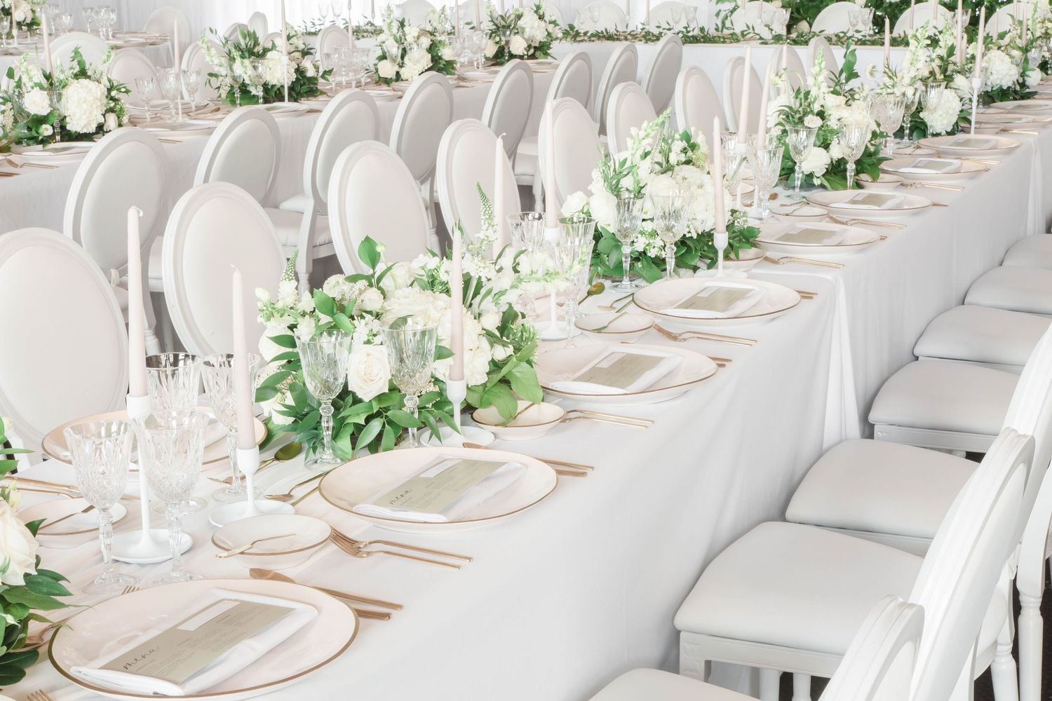 Elegant white wedding reception tables set with floral arrangements and crystal glassware.