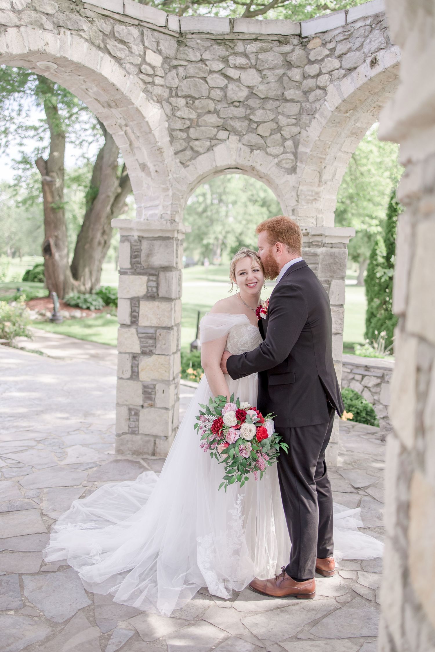 Wedding couple embraces under a series of stone archways in a garden setting.