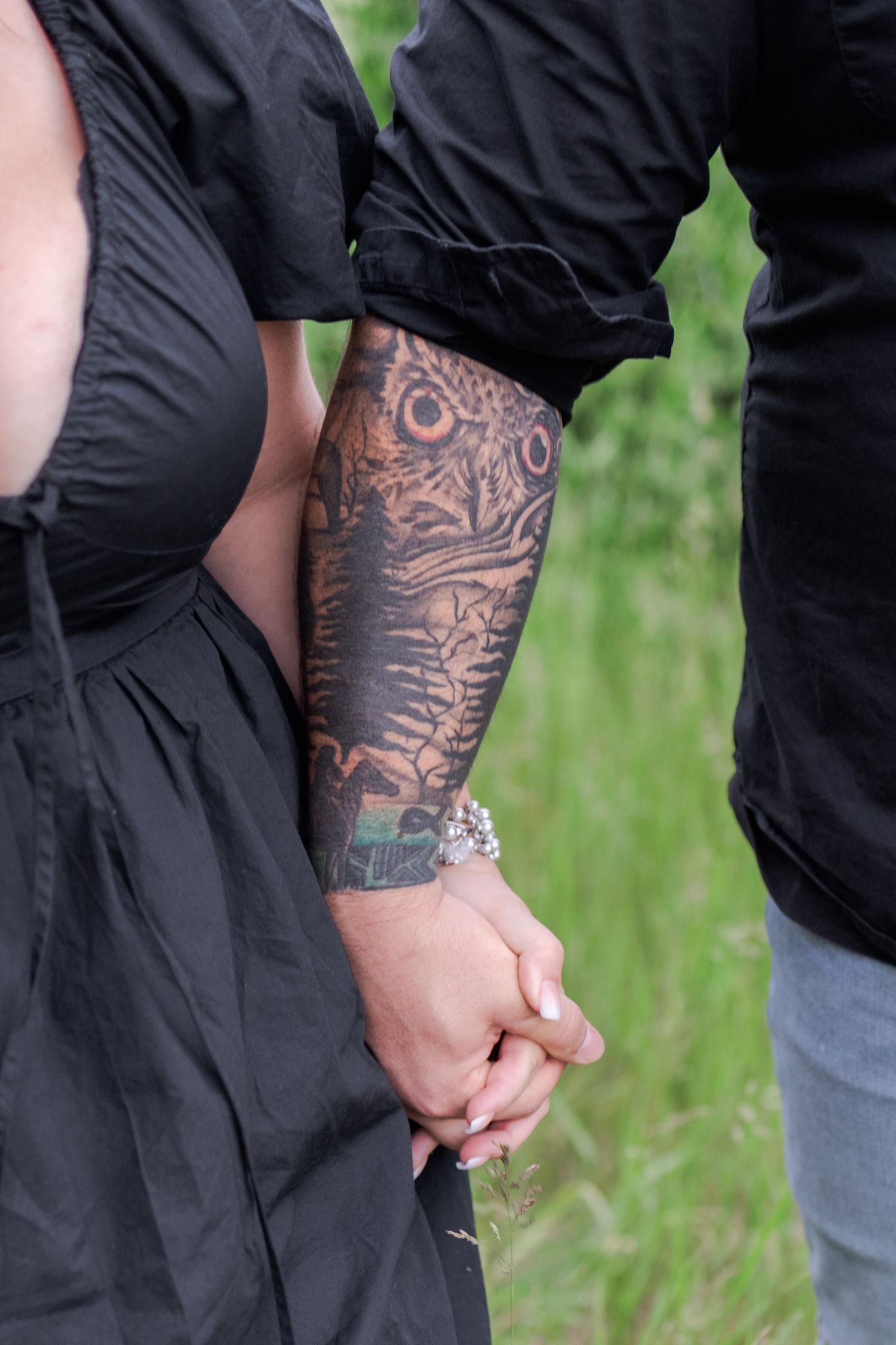 Close-up detail of tattooed arms and hands against black clothing in a field setting.