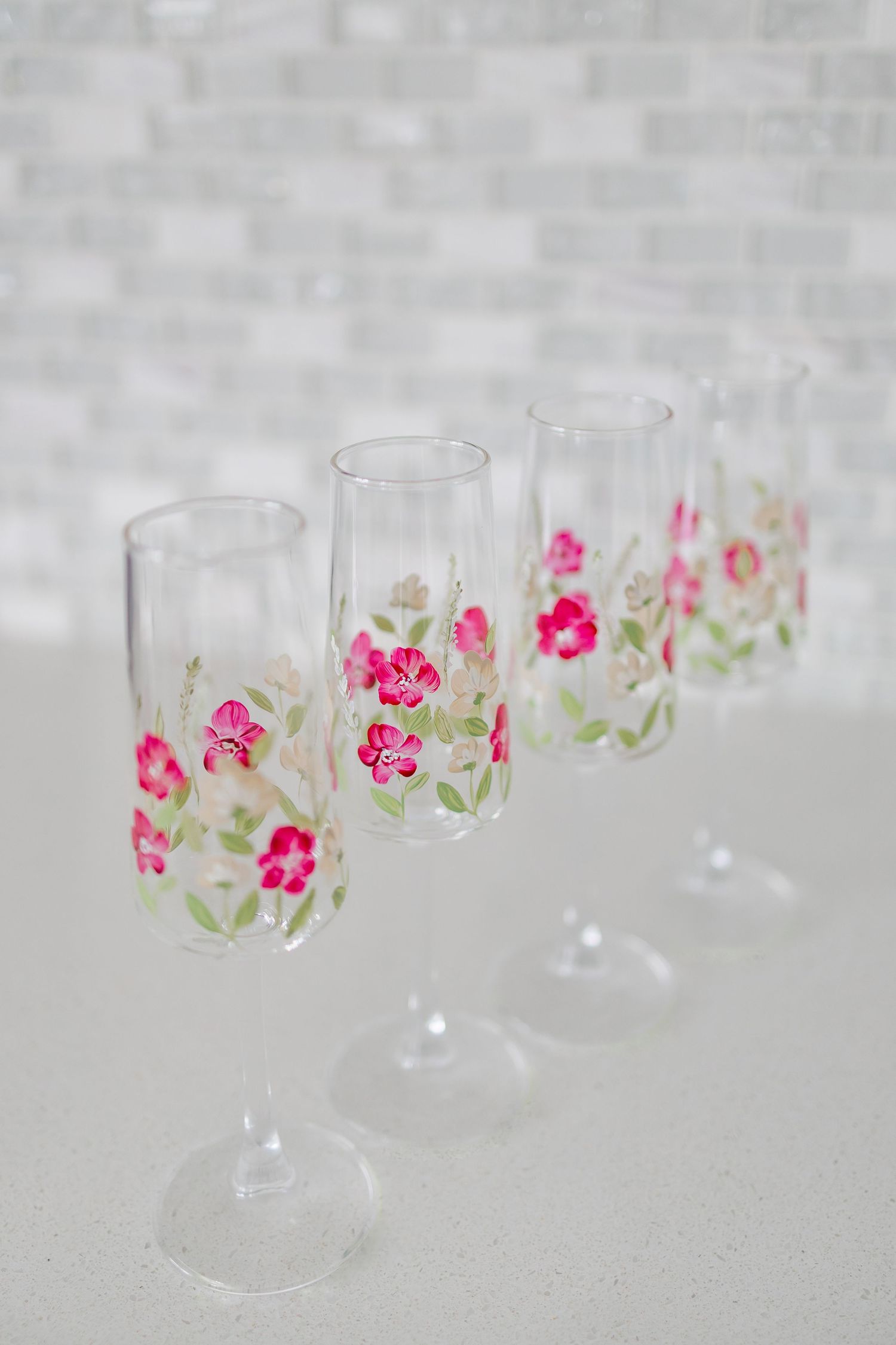 Clear glass goblets with delicate pink floral designs arranged in a row on a light gray background.