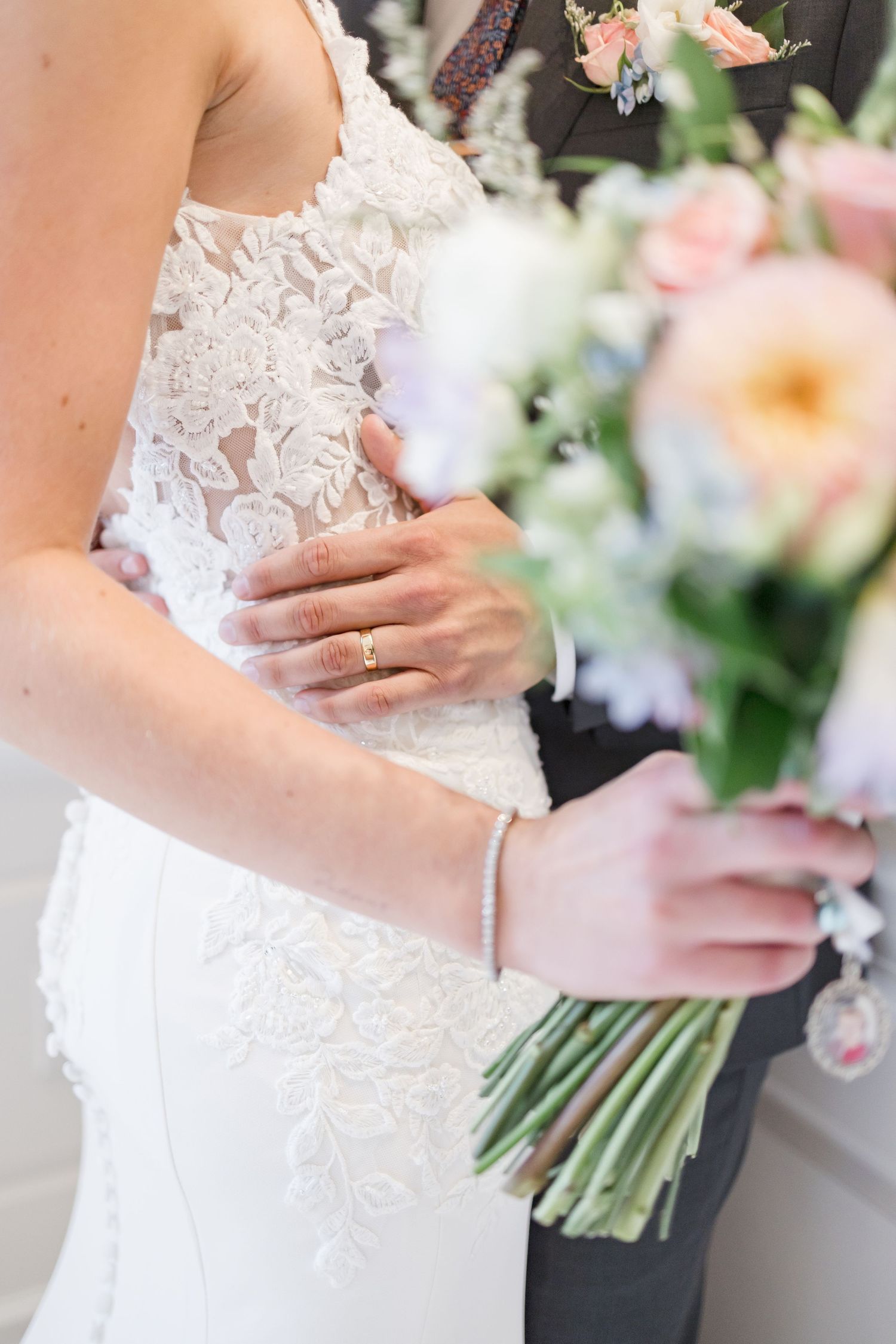 Close-up details of a lace wedding dress bodice with floral bouquet.