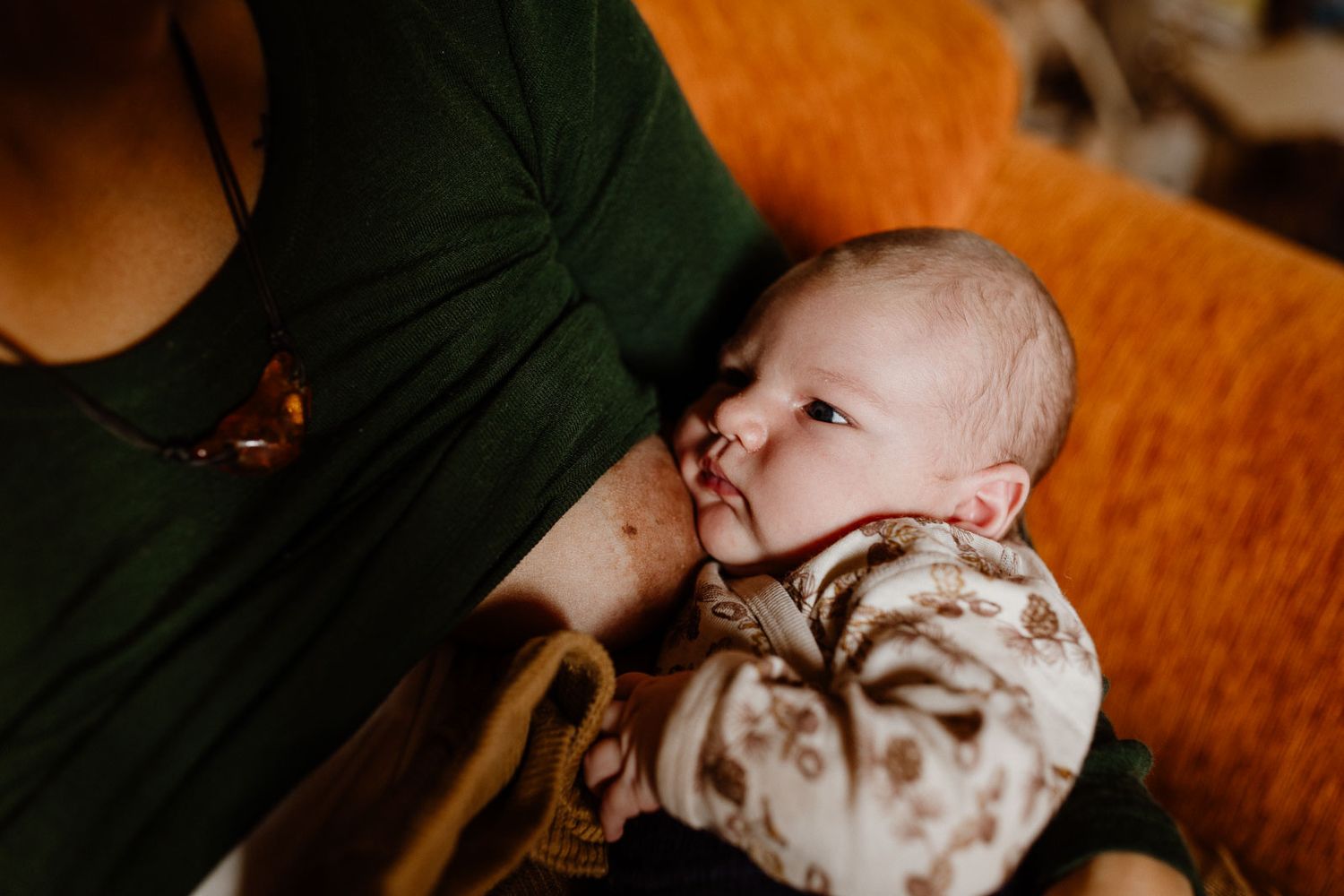 Baby in patterned onesie nursing while resting on an orange couch.