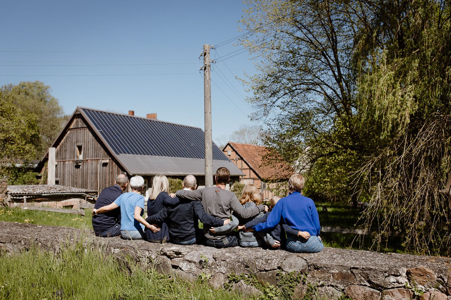 Group of people sitting together on stone wall overlooking rural houses.