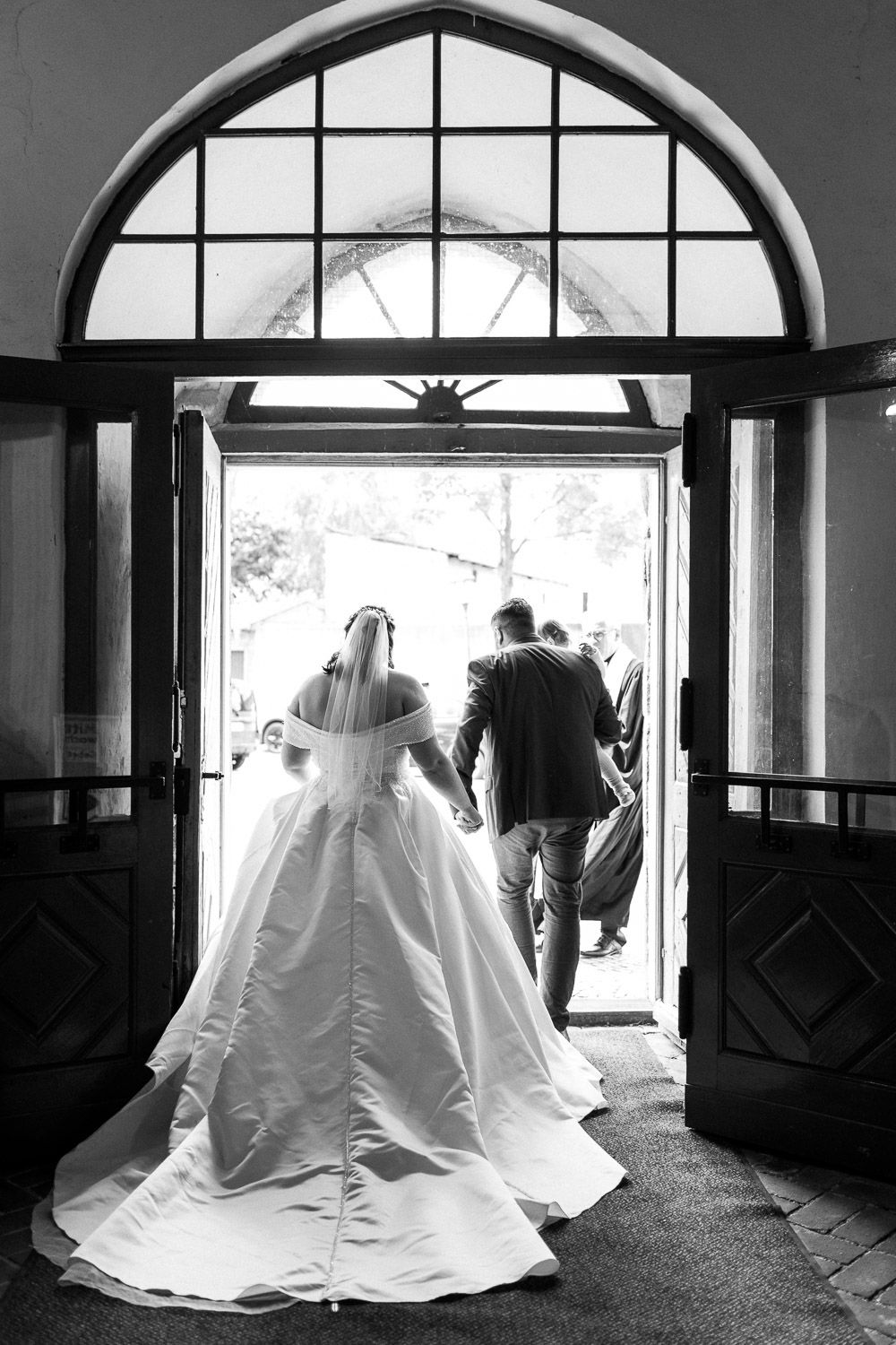 Black and white silhouette of couple exiting through arched doorway.