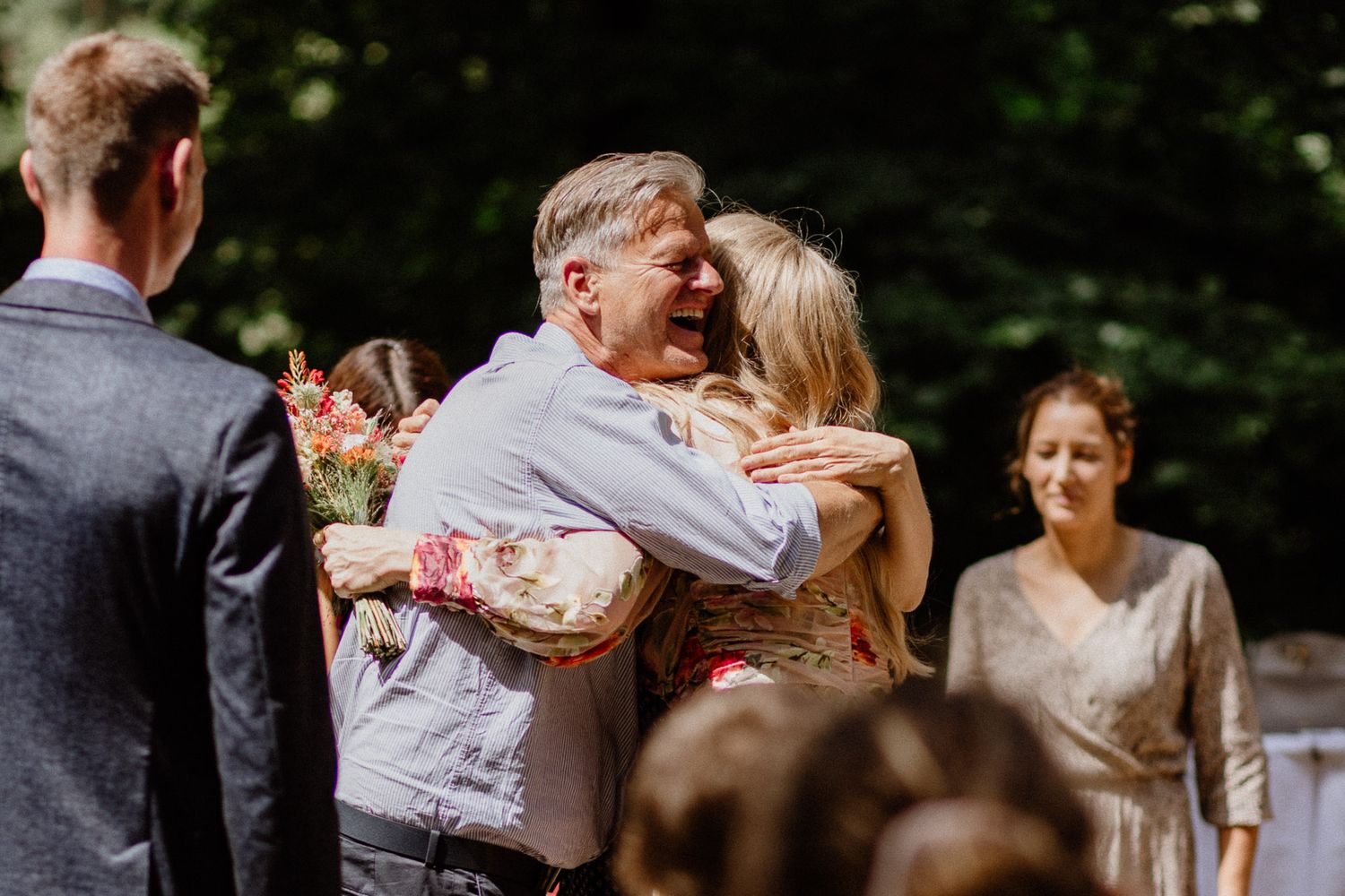Candid outdoor wedding moment with guests sharing joyful embrace.