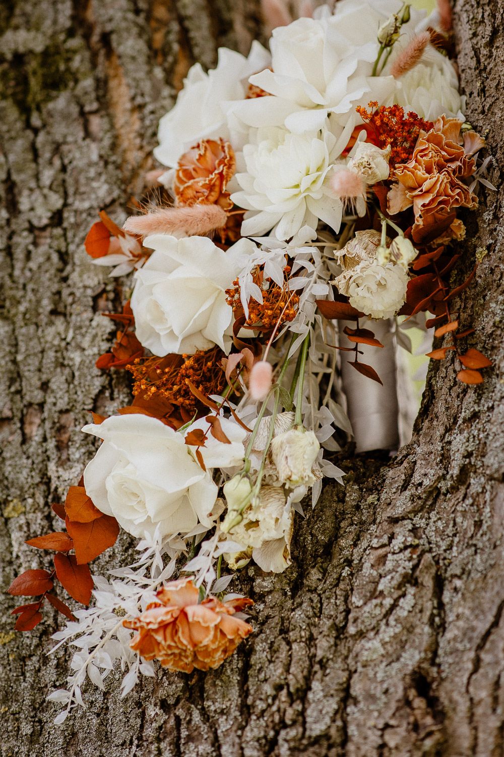 Romantic floral arrangement with white and orange blooms against tree bark texture.