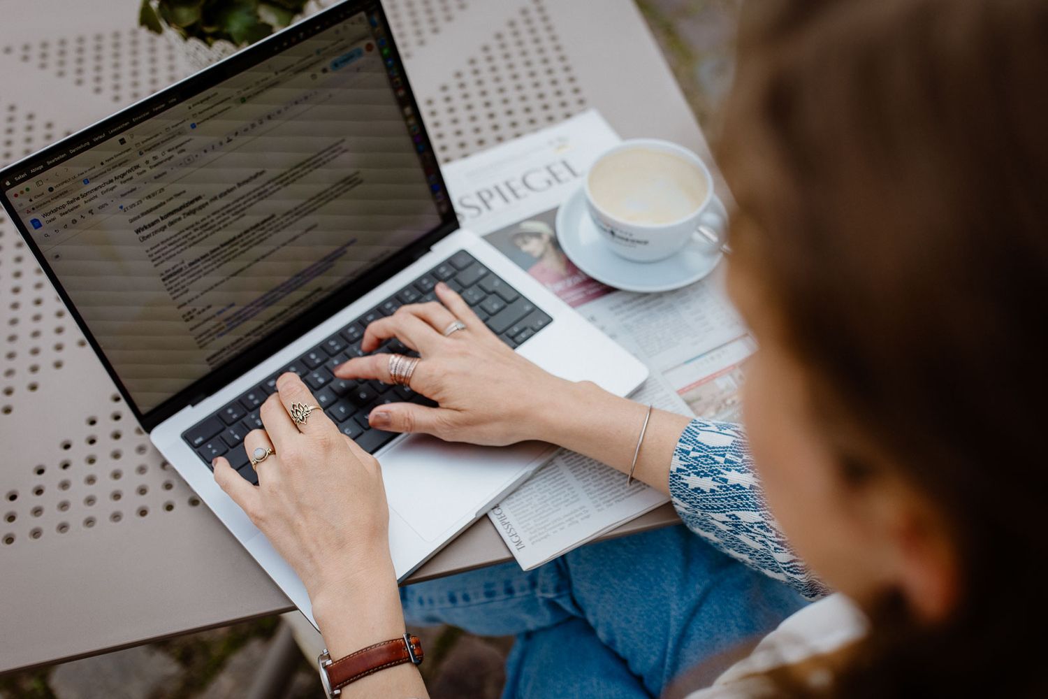 Hands typing on laptop keyboard with coffee cup on desk while working.