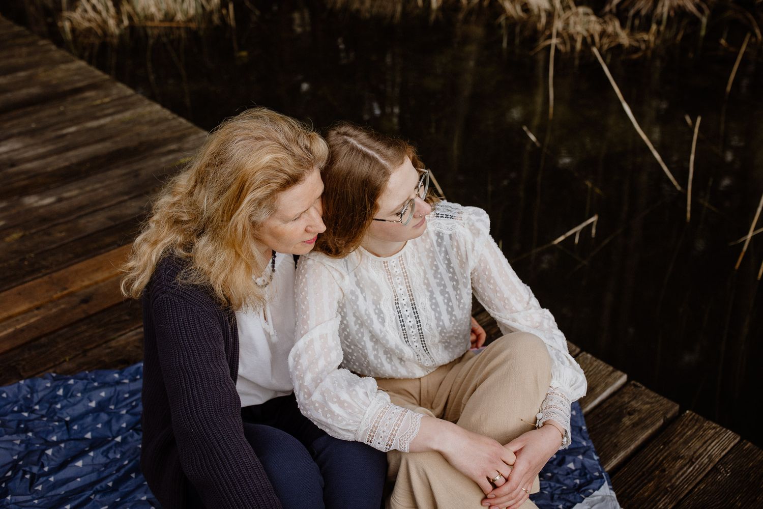 Two people share intimate moment while sitting on wooden dock with blue blanket.