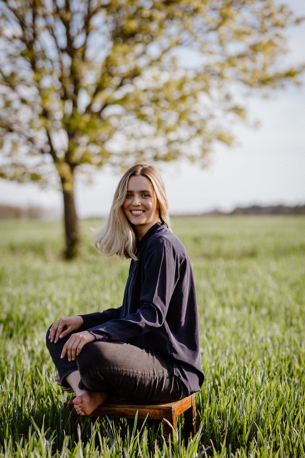 Joyful outdoor portrait sitting in tall grass with a tree in the background during golden hour.