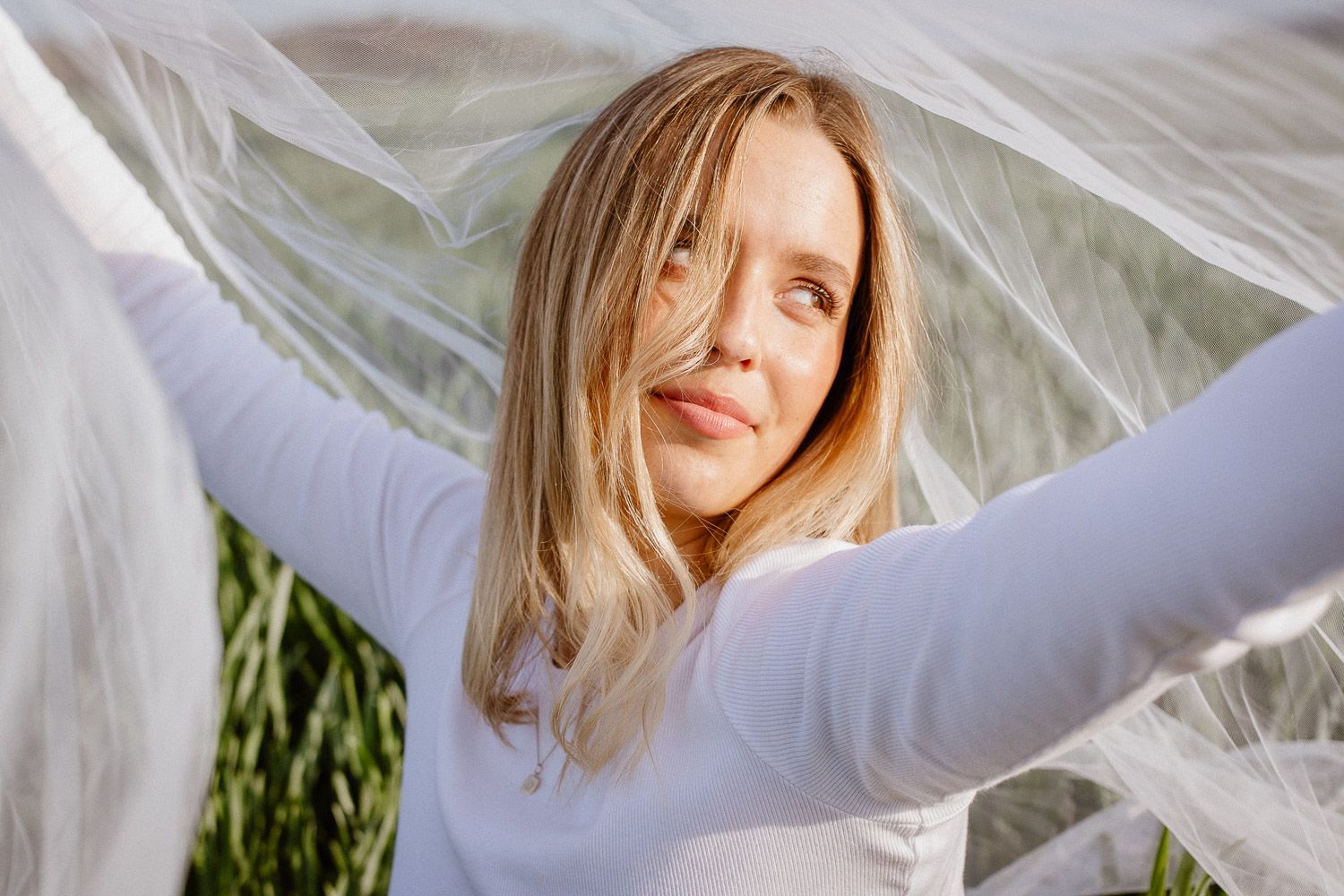 Artistic portrait with sheer white fabric creating ethereal effect against natural backdrop.