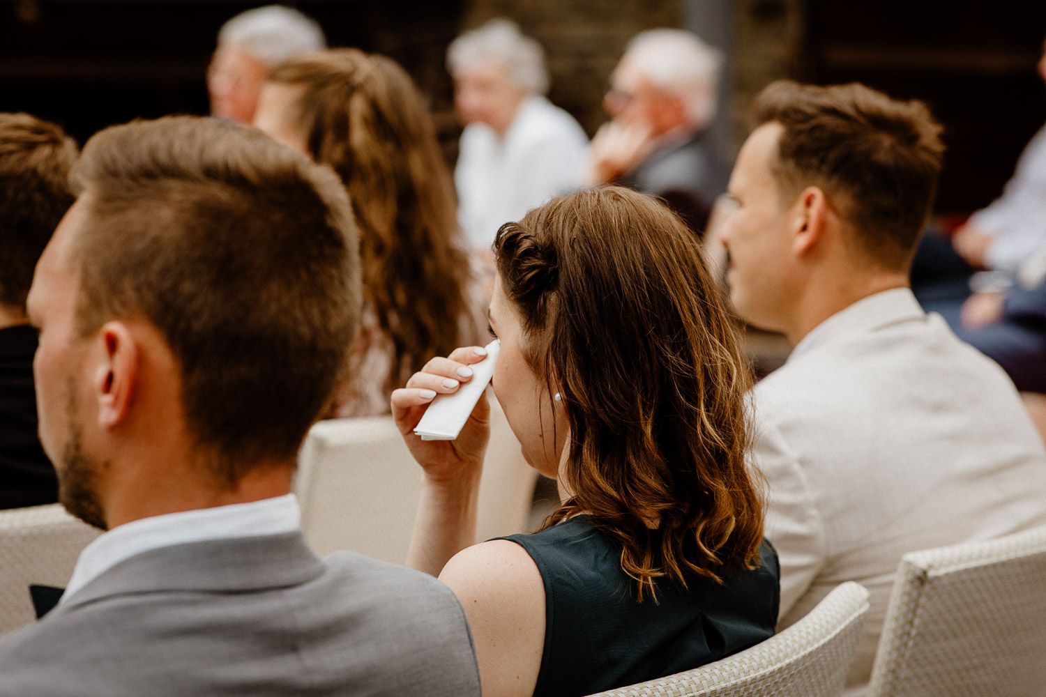 Wedding guests seated in white chairs during an indoor ceremony.