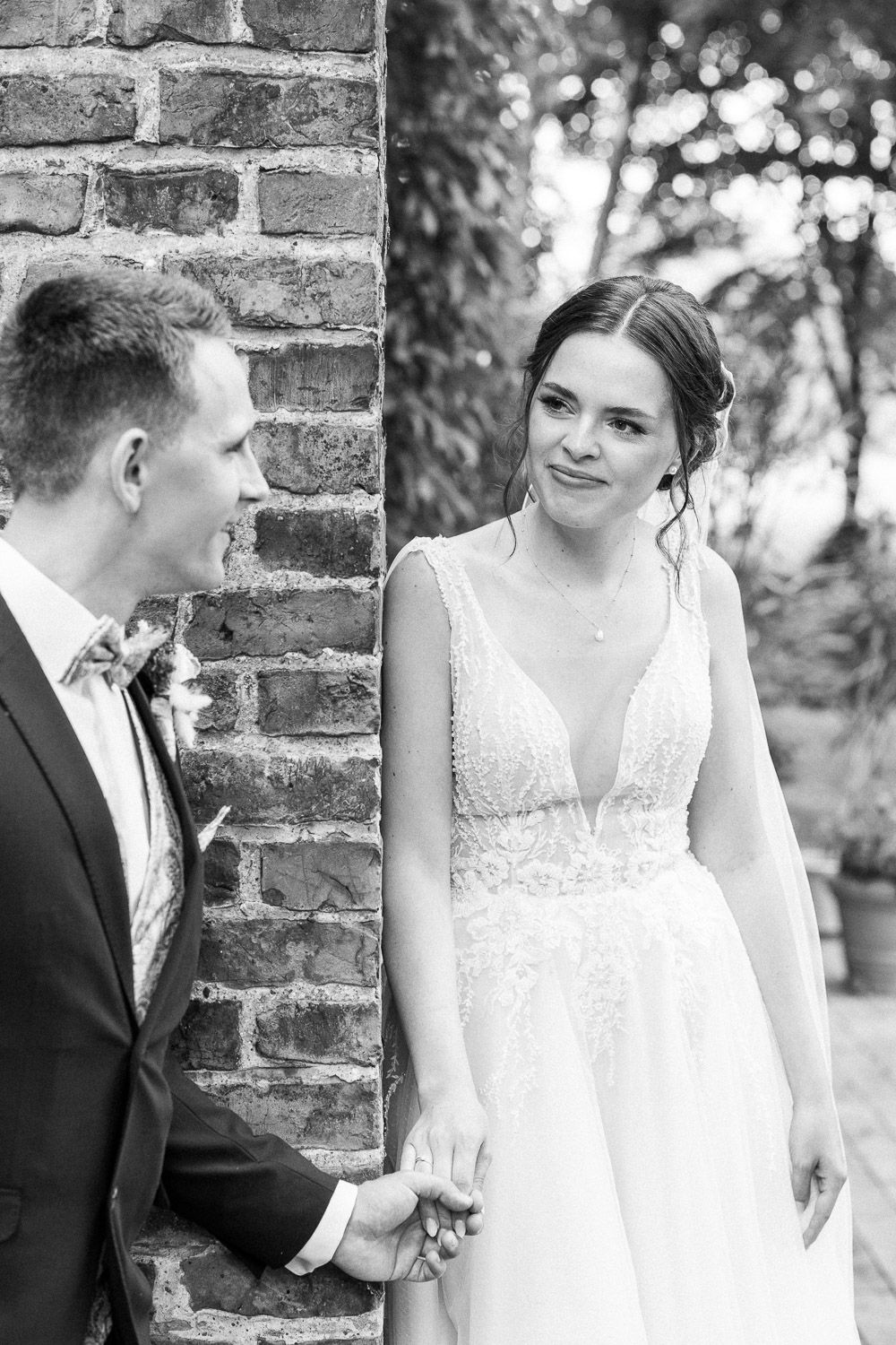 Black and white portrait of a couple sharing a romantic moment against a brick wall background.