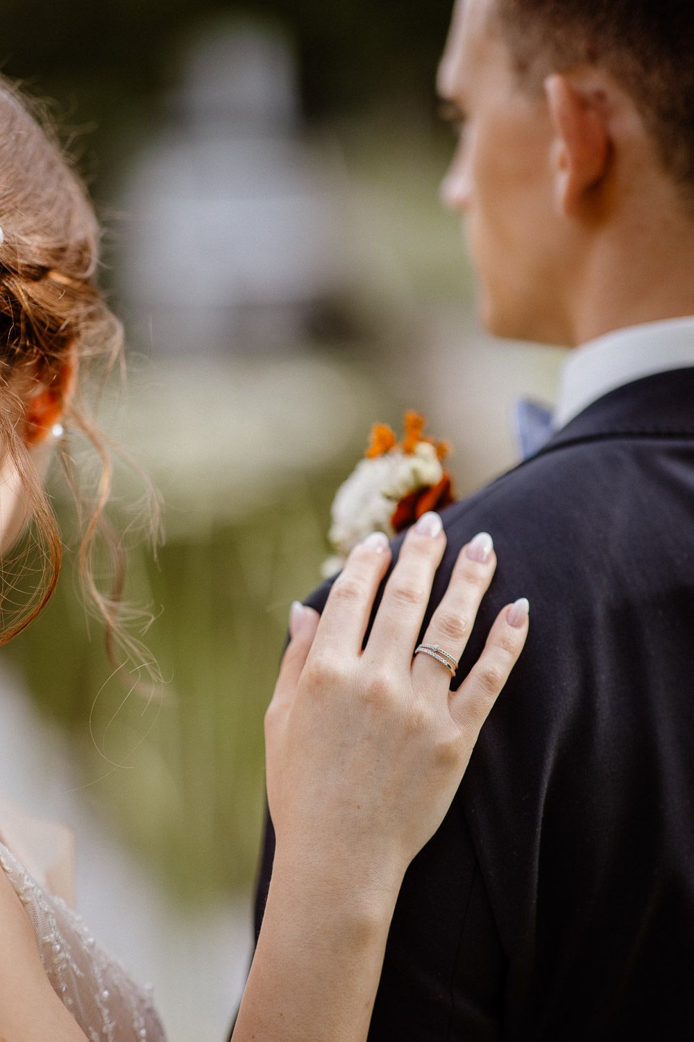 Close-up of a hand wearing a wedding ring resting on a dark suit jacket.