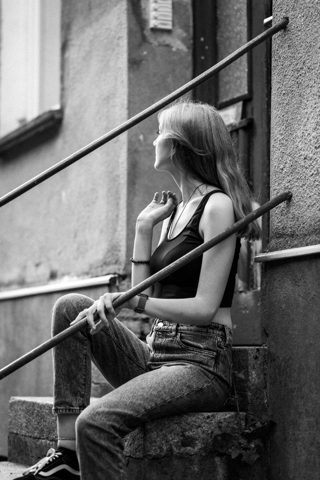 Black and white photo of someone sitting on concrete steps near metal railing.