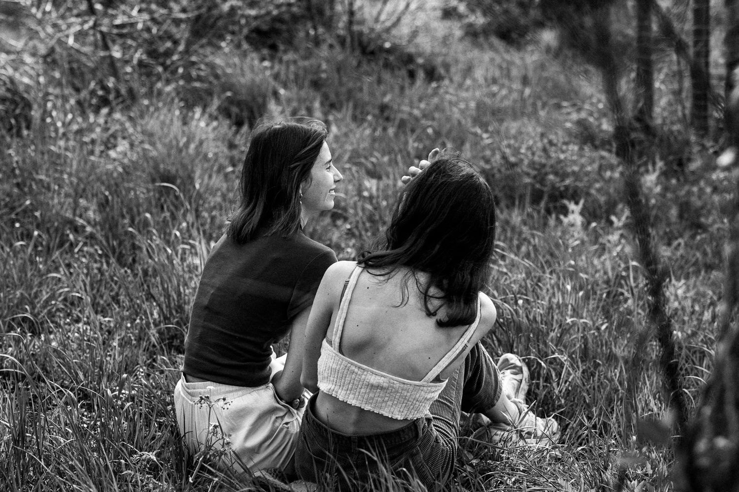 Two people sitting together in a grassy meadow captured in black and white photography.