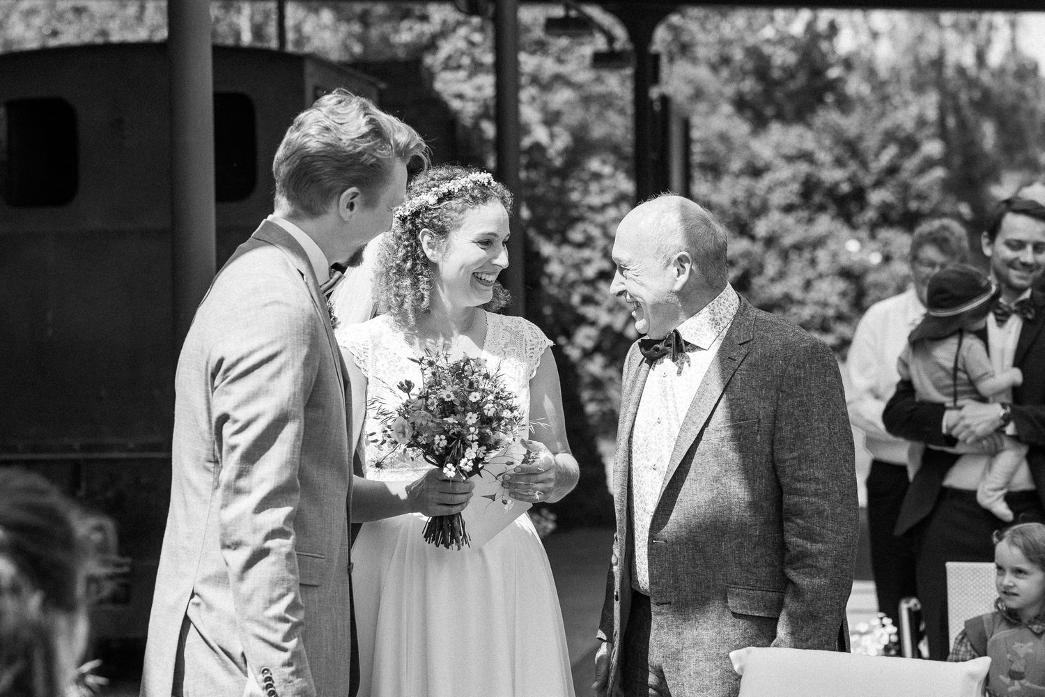 Wedding ceremony guests gathered outside in formal attire on a sunny day.