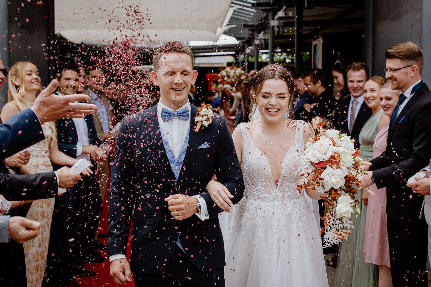 Newlyweds walk through a shower of red confetti during their wedding celebration.