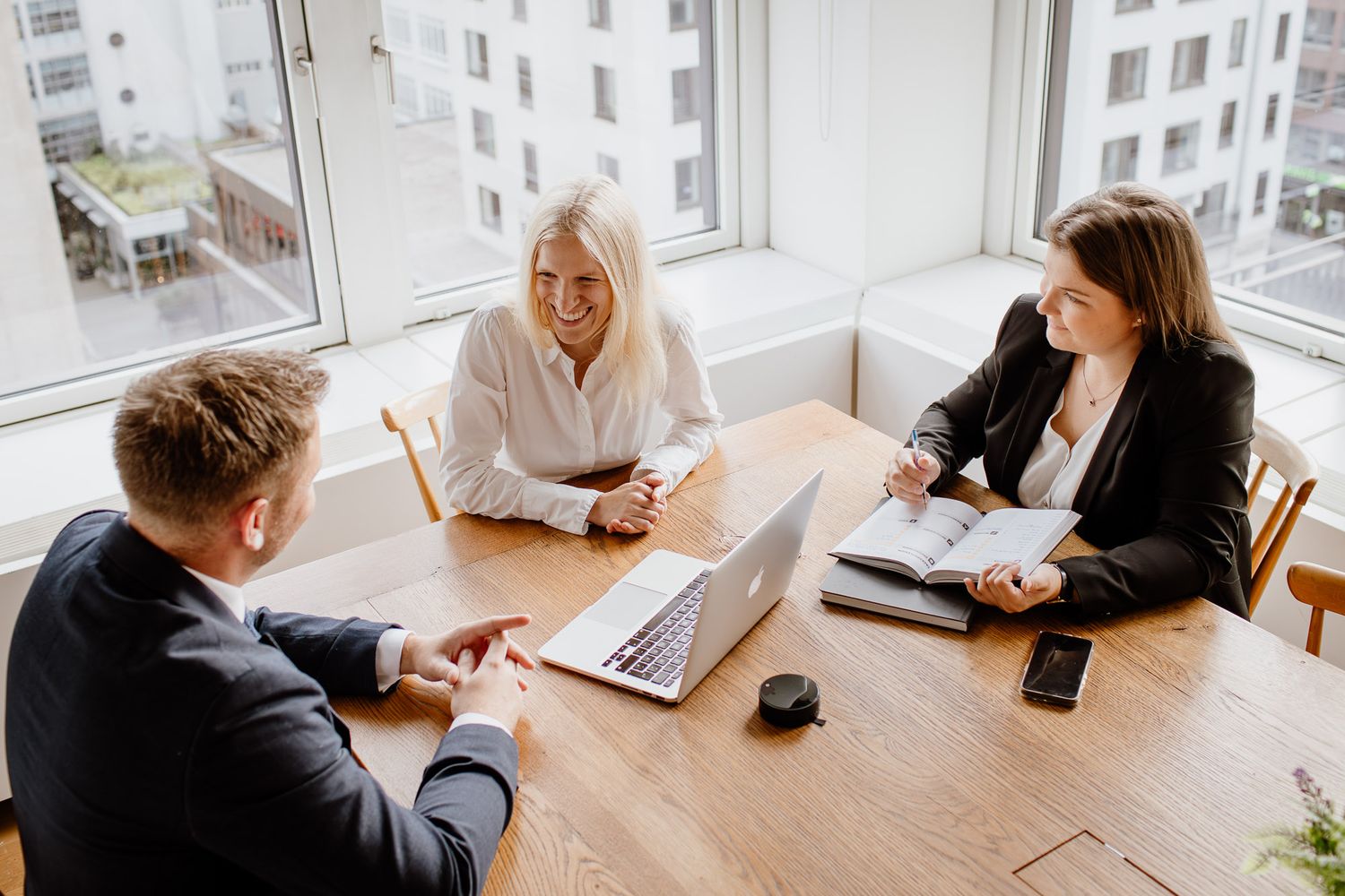 Business meeting in modern office with people gathered around wooden table.