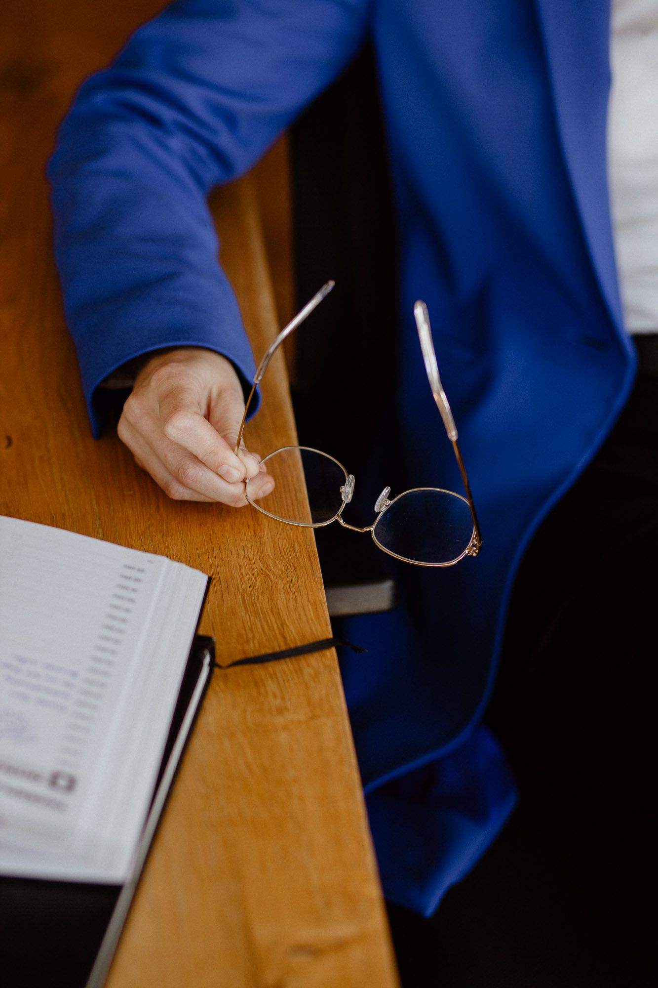 Close-up of hands in blue sleeves handling eyeglasses on a wooden desk.