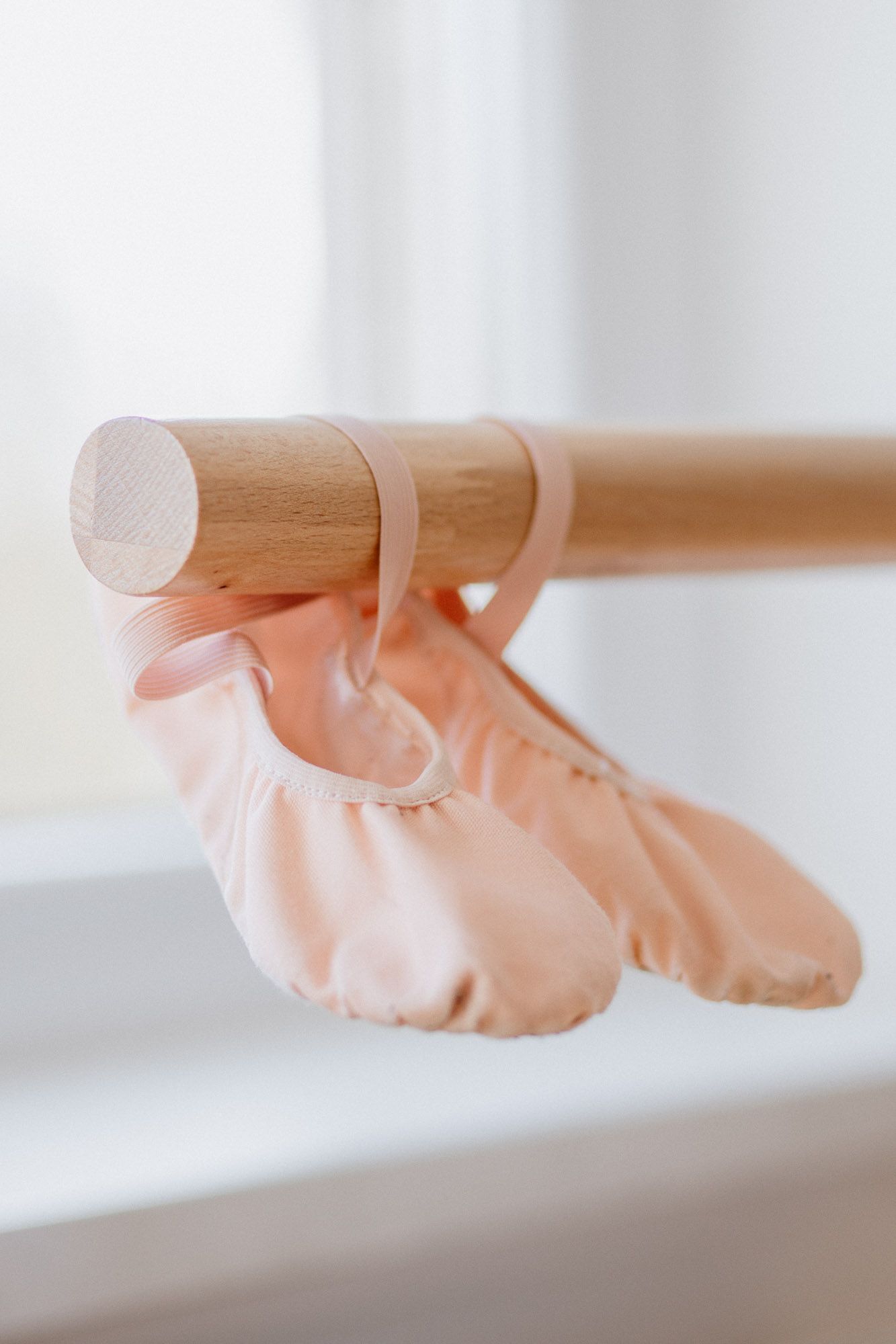 Ballet shoes in soft pink satin are positioned in an artistic arrangement against a bright white background.