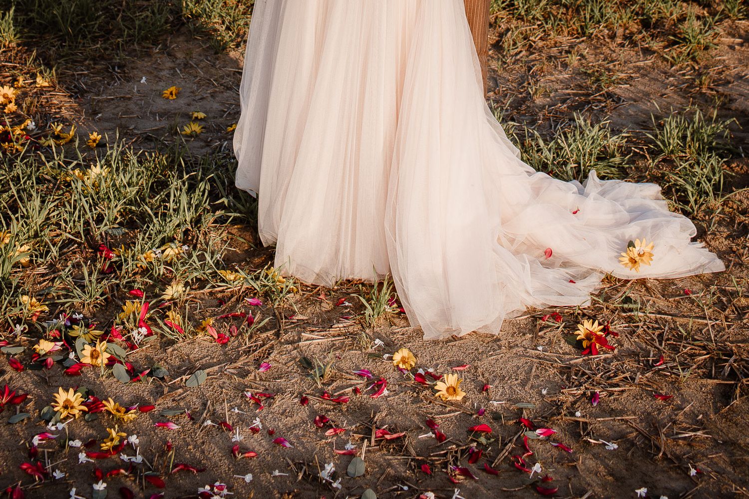 A flowing white wedding dress train drapes over fallen autumn leaves scattered on the ground.