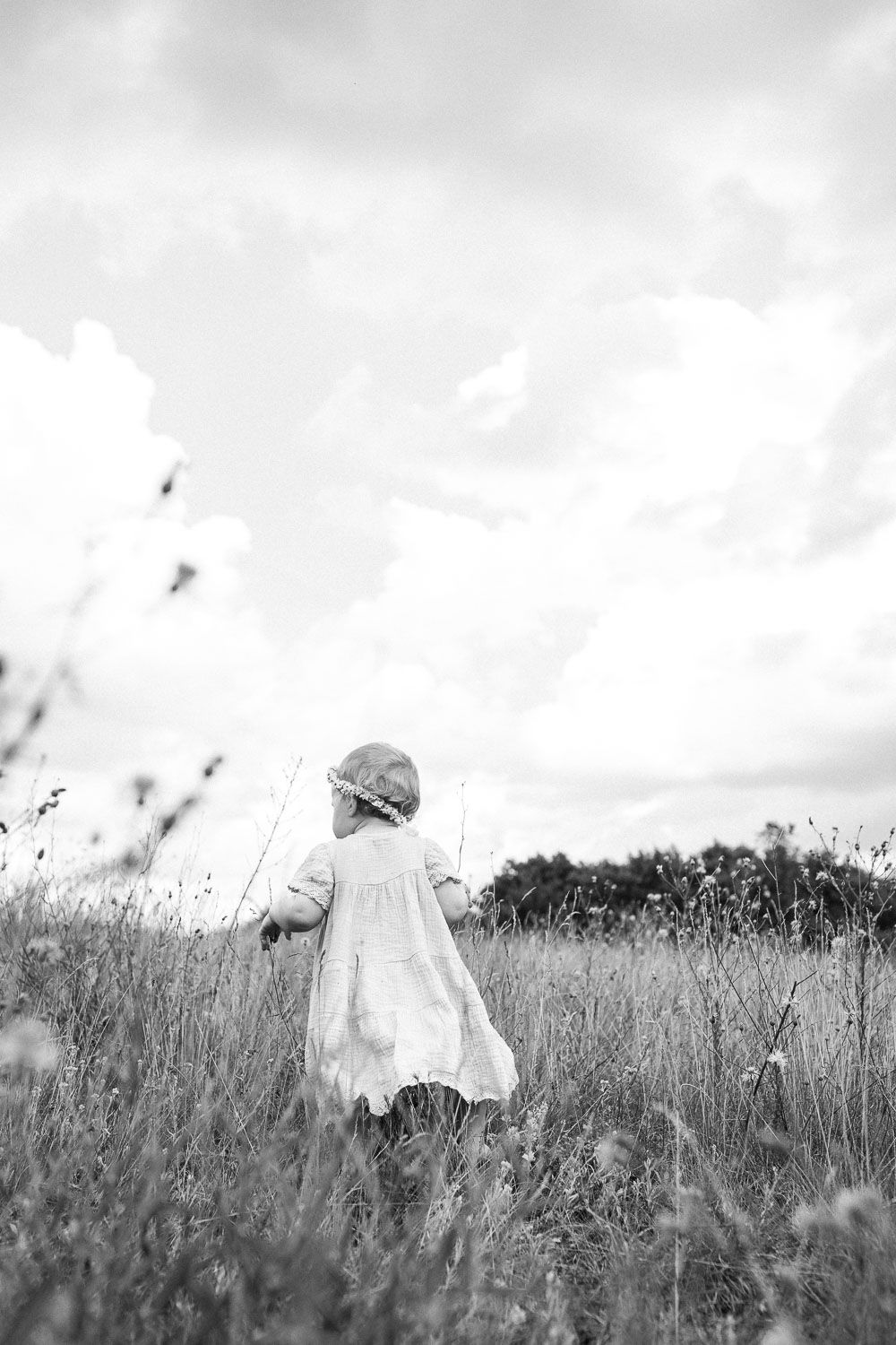 A dreamy black and white photo of a small figure in a white dress standing in a field of tall grass.