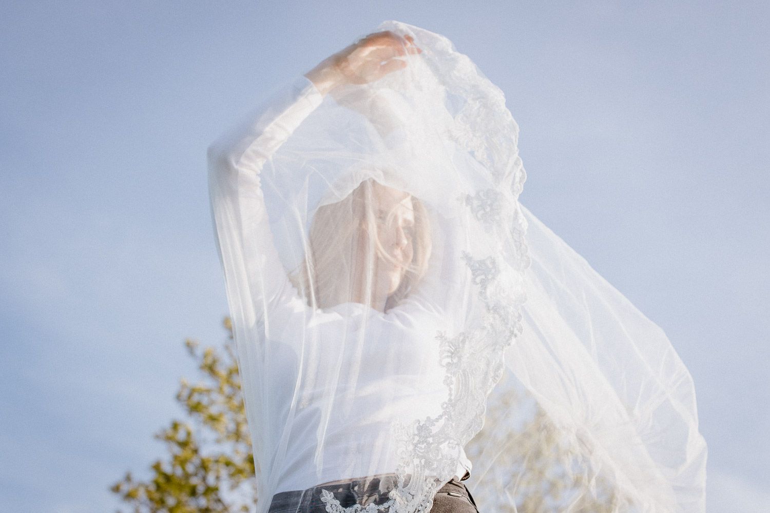 Ethereal white veil flowing against a blue sky with tree branches visible in the background.