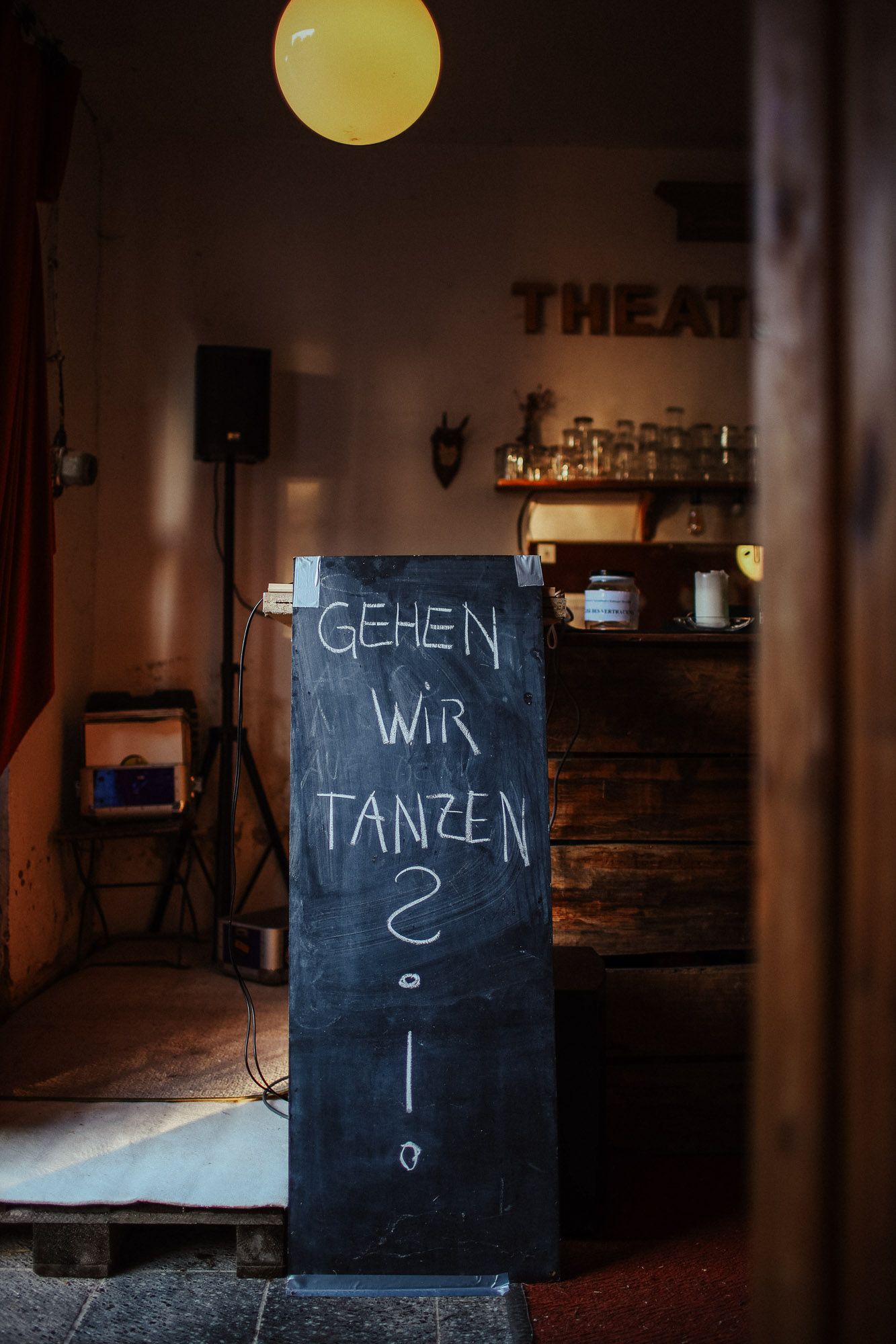 A dark chalkboard sign with German text 'Gehen wir tanzen' in a dimly lit venue.