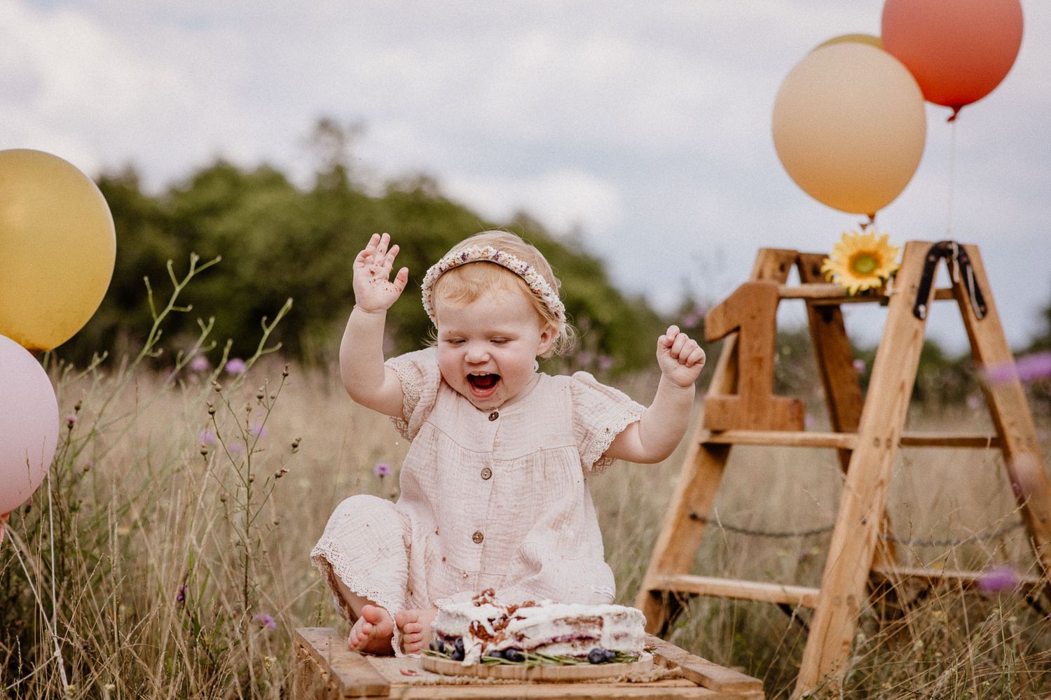 Festive outdoor scene with colorful balloons and cake on rustic wooden platform.