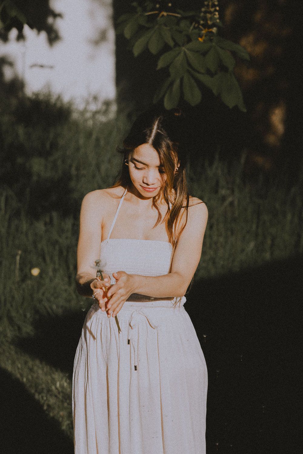 Figure in a flowing white summer dress stands in a garden at golden hour with soft natural lighting.