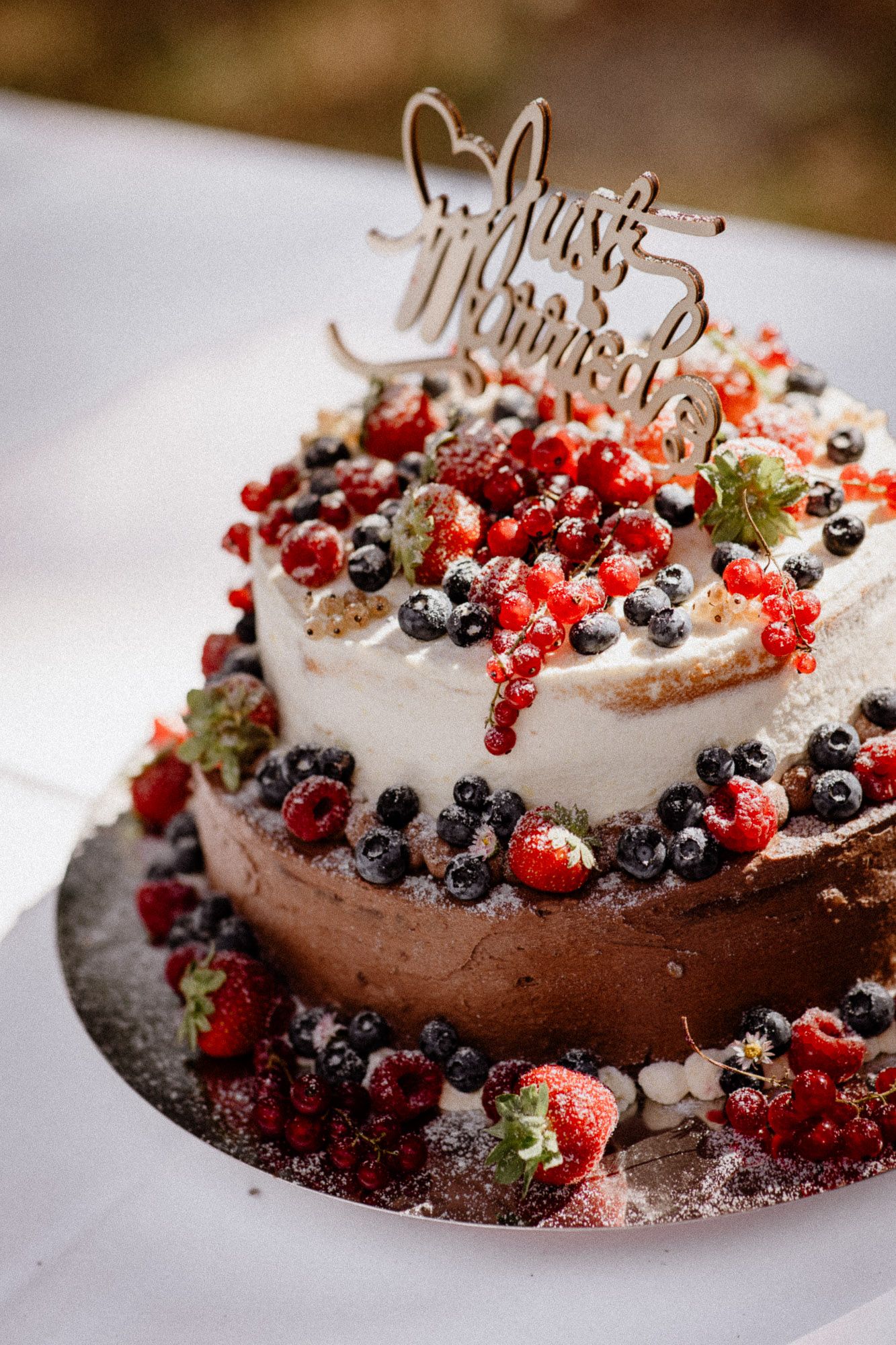 Two-tiered wedding cake decorated with fresh berries and Just Married topper.