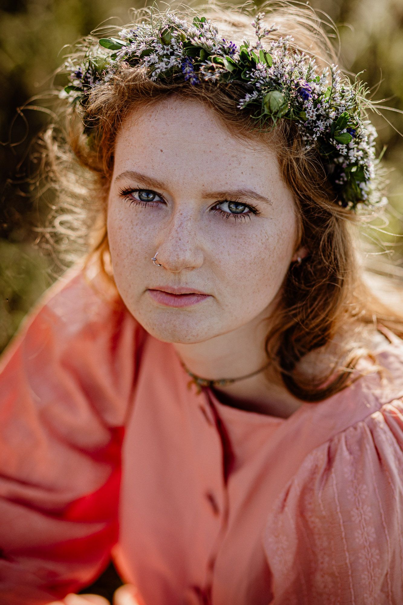 Portrait wearing a flower crown with purple blooms and greenery against soft natural lighting.