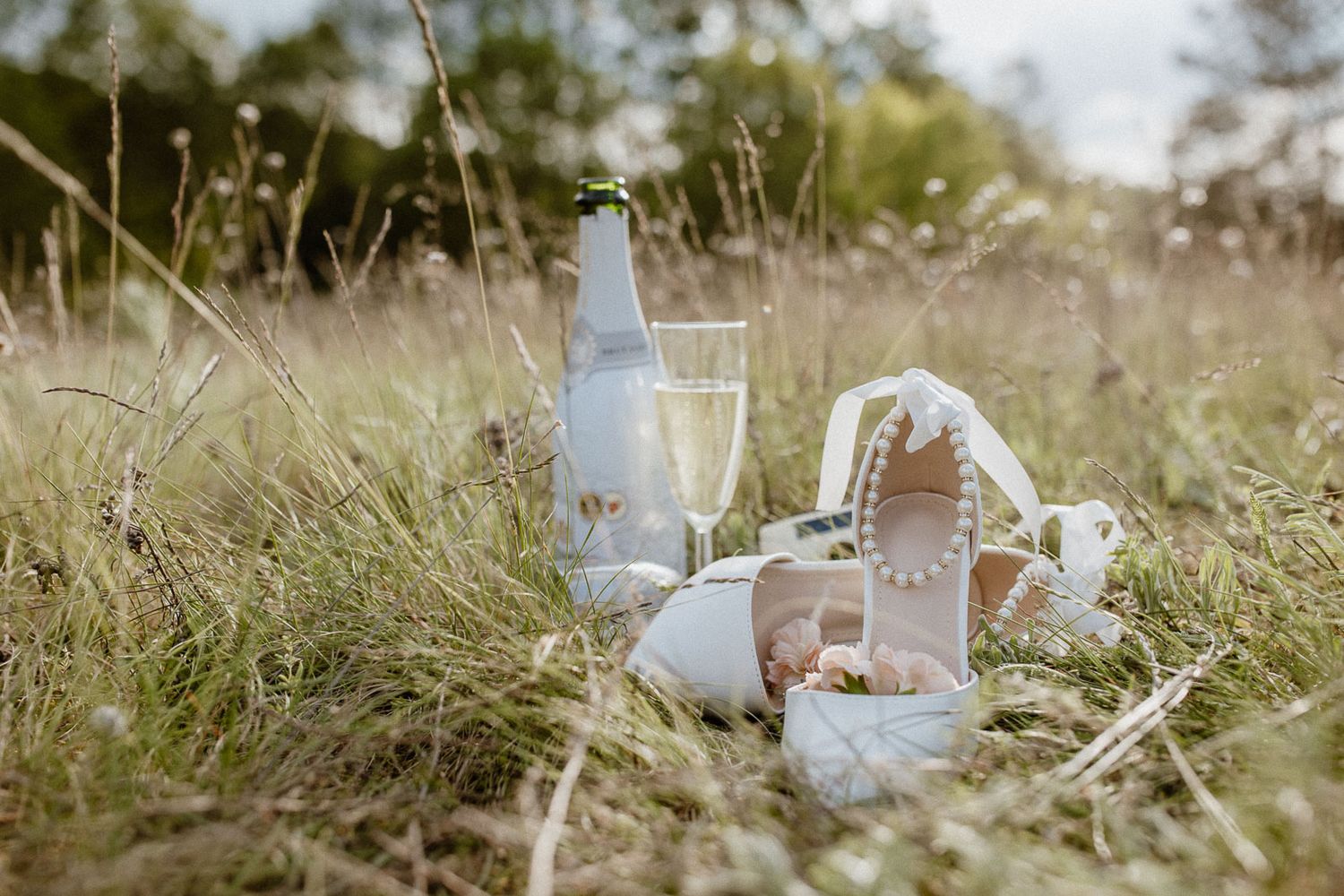 Romantic picnic setup in tall grass with glass milk bottles, white ceramics, and fresh bread.