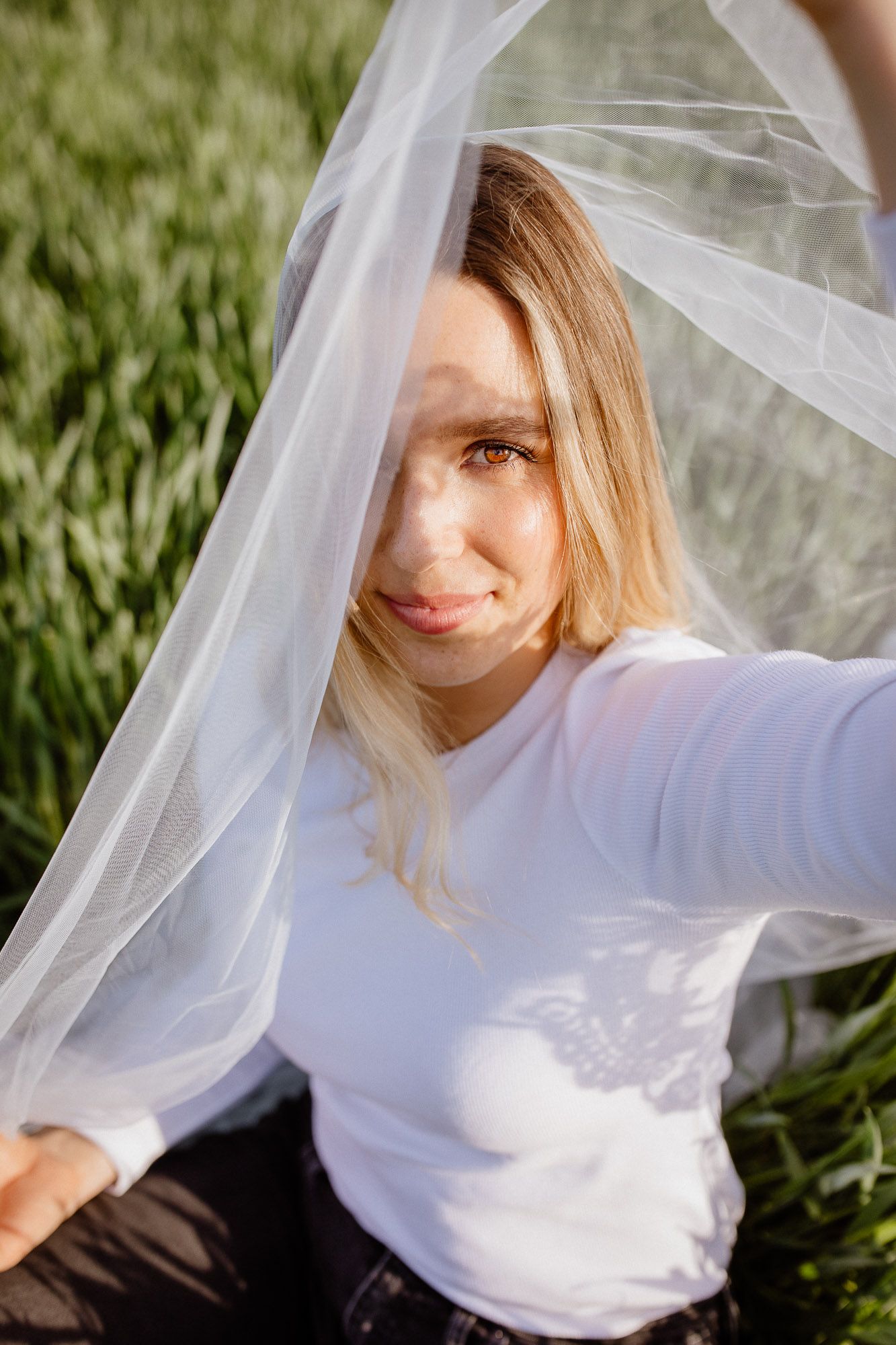 A dreamy portrait series of a person wearing white against grass, with a sheer veil flowing in the breeze.