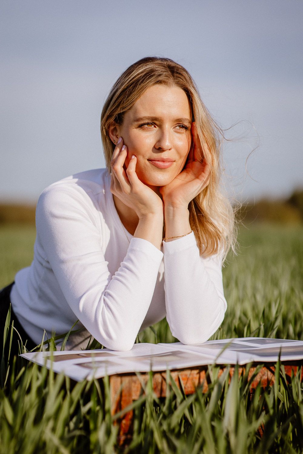 Woman resting in grassy field with hands on face while looking at camera.