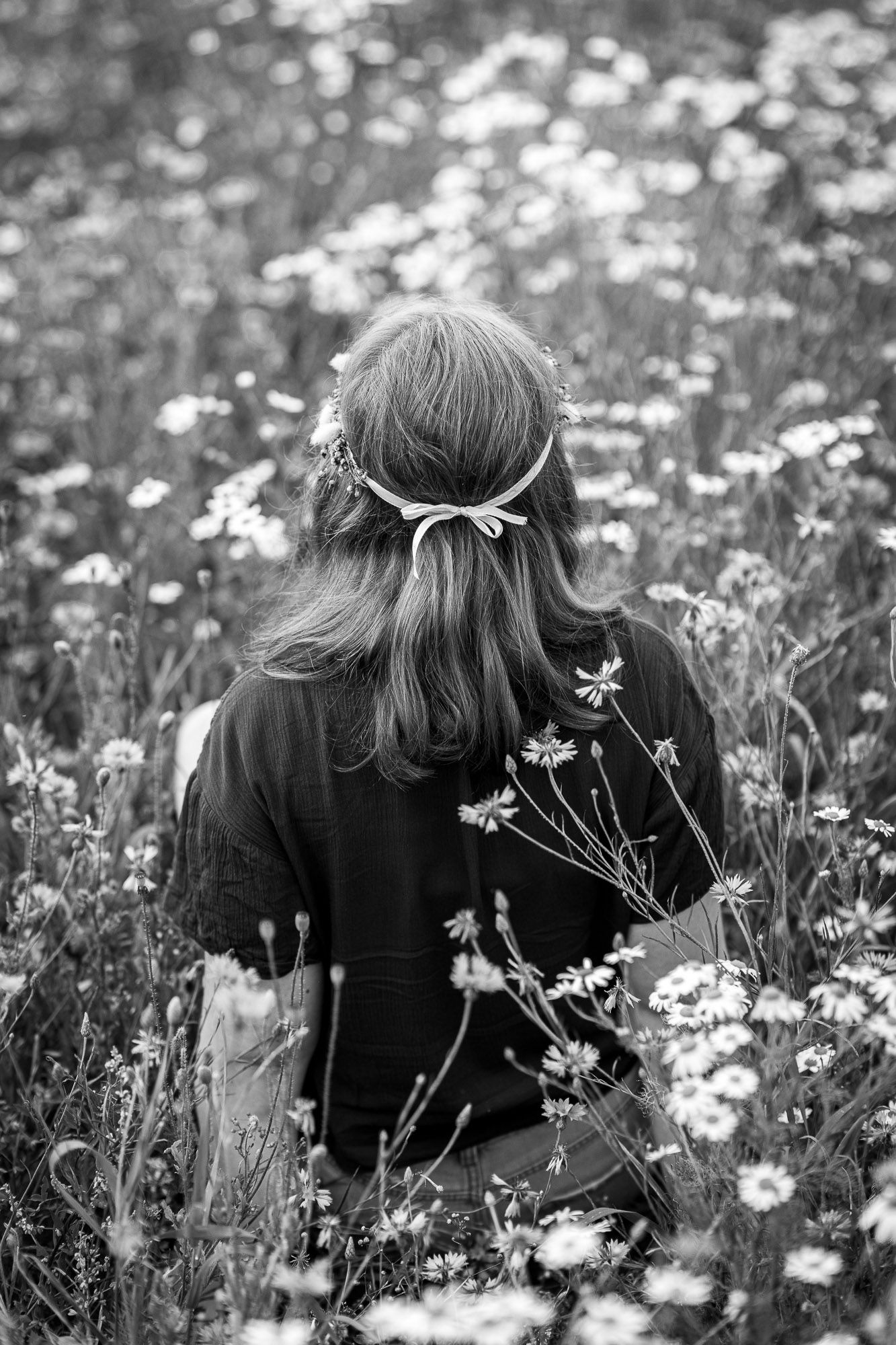 A person wearing black lies among a field of white daisies in a black and white artistic photograph.